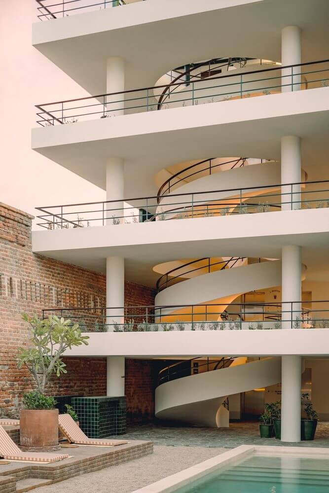 Baja Club, Mexico — Spiral ramp descending through white modernist atrium with cylindrical columns, brick courtyard, and pool below.