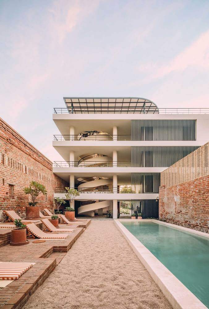 Baja Club, Mexico — Modernist courtyard with turquoise pool, terracotta loungers, brick walls, and multi-level white building with solar panels and metal railings.