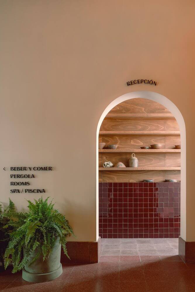 Baja Club, Mexico — Arched reception nook with terracotta tiles, wooden shelving, warm plaster walls, and potted fern in minimalist hospitality design.