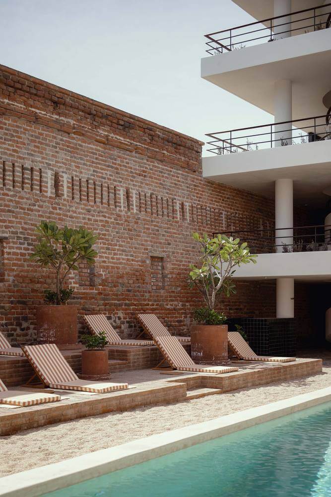 Baja Club, Mexico — Modernist courtyard with striped loungers, terracotta planters, red brick walls, and turquoise pool reflecting minimalist architecture.