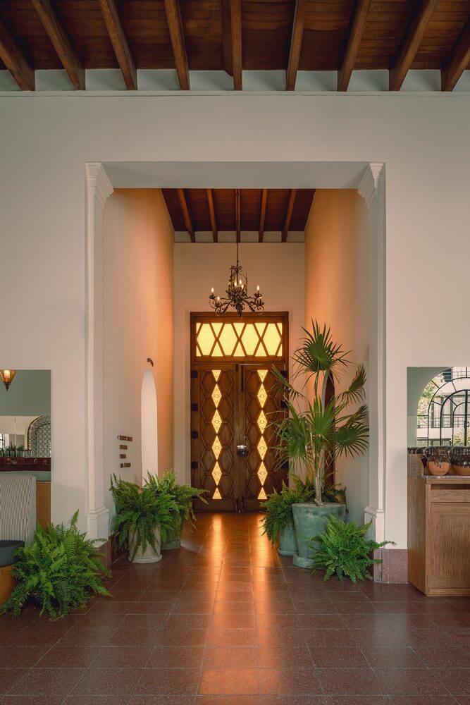Baja Club, Mexico — Illuminated wooden doors with geometric patterns frame a warm entry hall with exposed beam ceiling, terracotta floors, and potted palms.