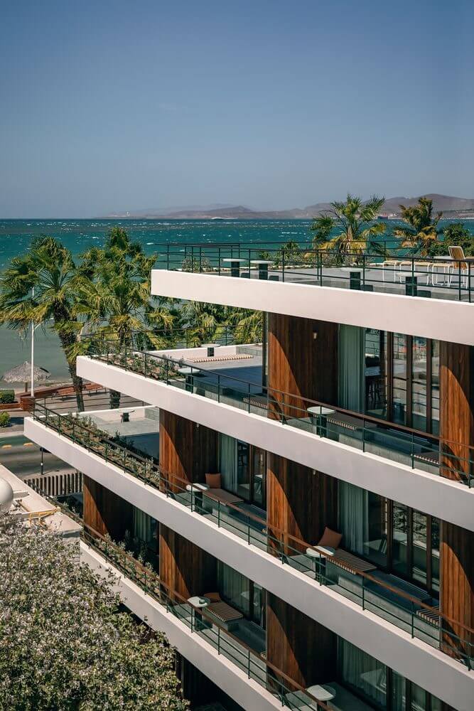 Baja Club, Mexico — Modernist oceanfront terraces with white cantilevers, teak accents, and turquoise sea views framed by palm trees.