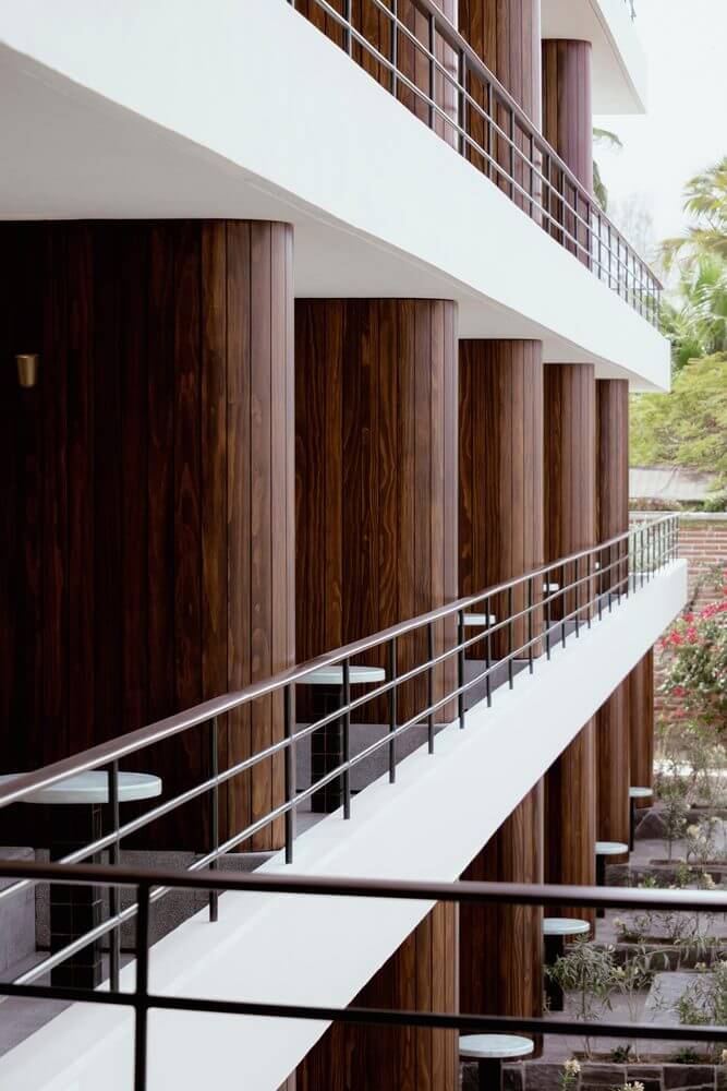 Baja Club, Mexico — Curved white balconies with dark wood column details and metal railings overlooking lush tropical grounds, modernist hospitality architecture.