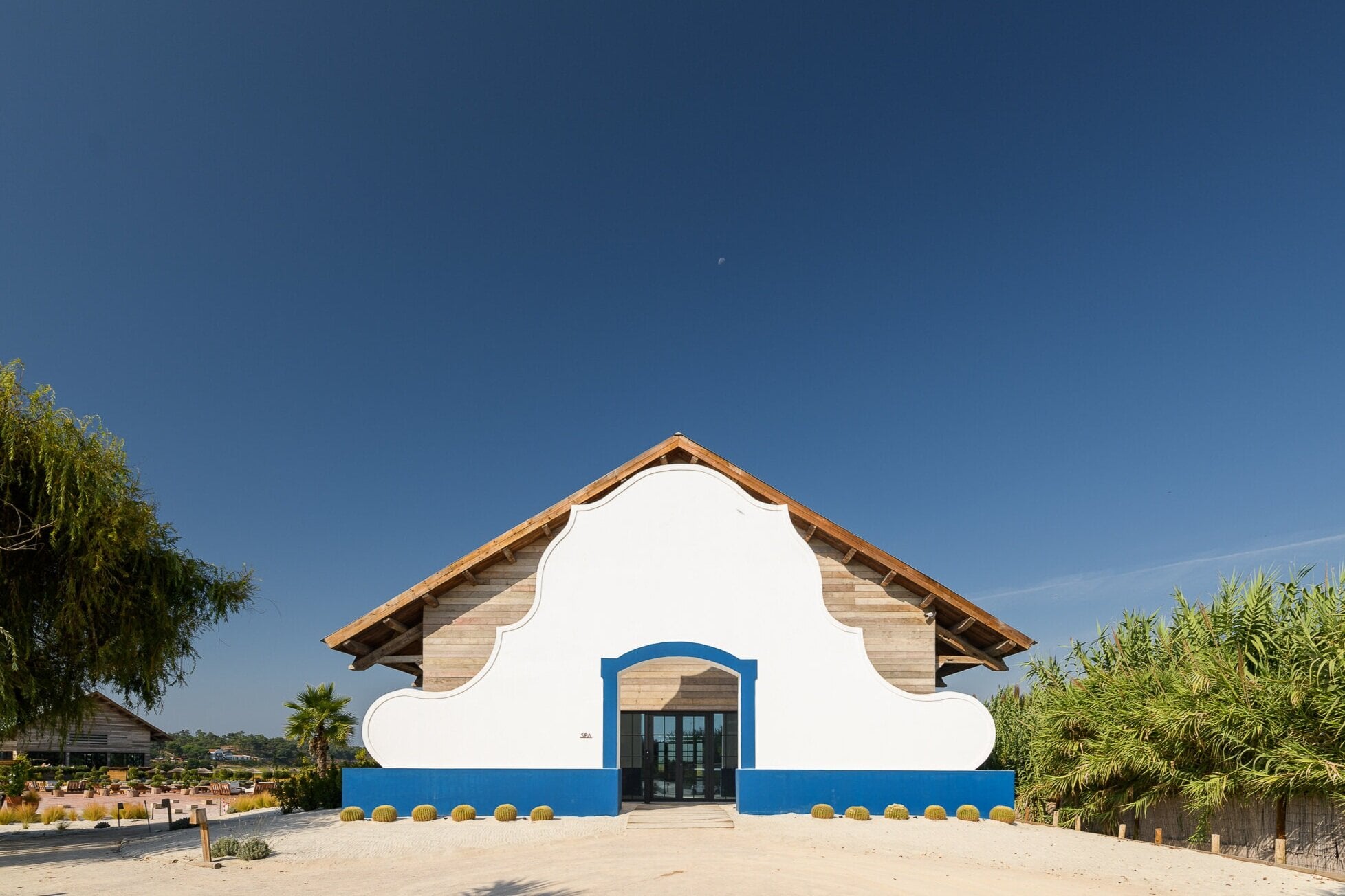 Quinta da Comporta, Portugal — Whitewashed curved facade with cobalt blue base and entrance, barrel-tile roof, desert landscaping, modern minimalist architecture.