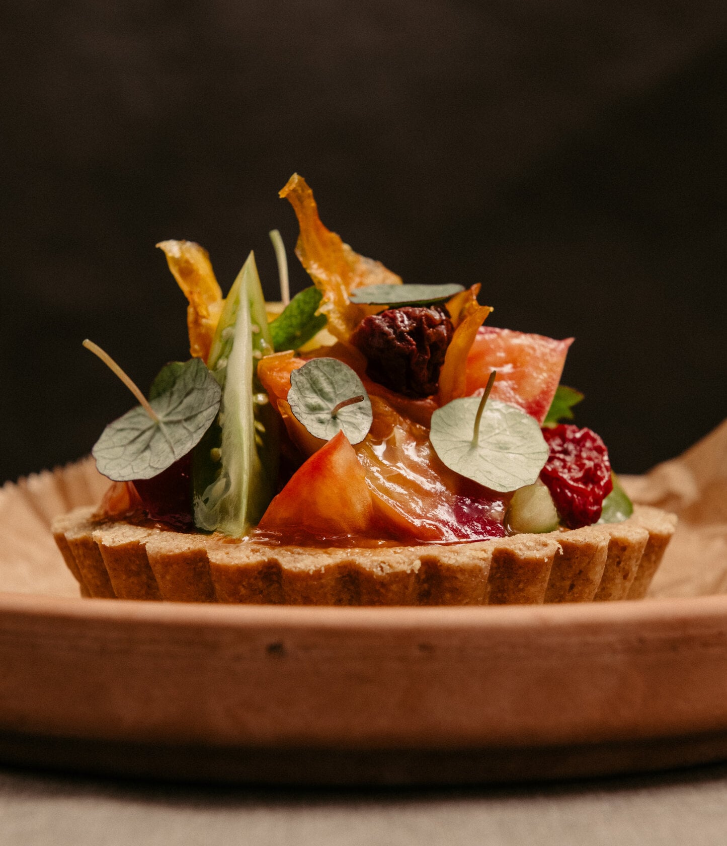 Dóttir & Hotel Bar, Europe — Plated tart with roasted vegetables, beetroot, crispy golden shards, and physalis leaves on warm ceramic, minimalist fine dining presentation.