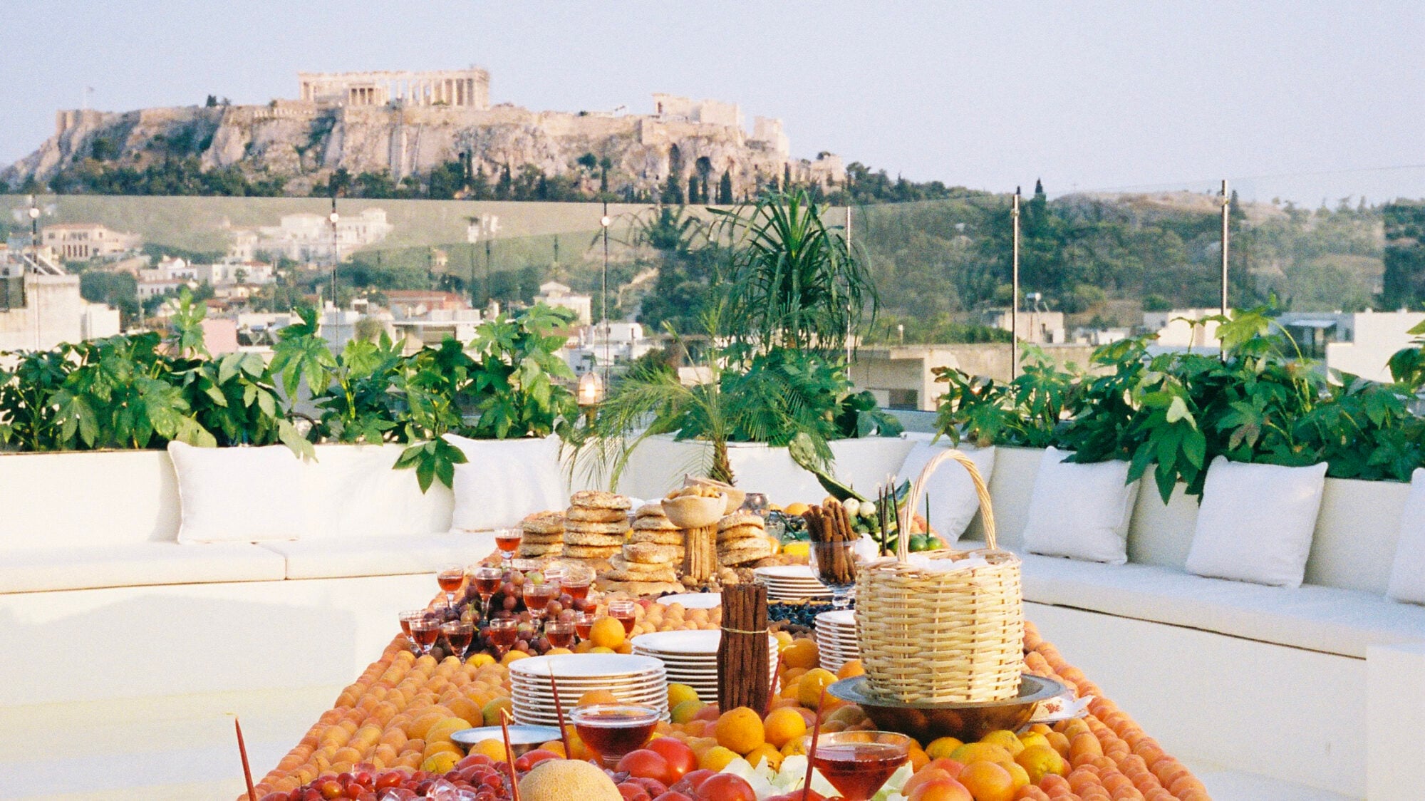 Rooftop Cocktail Bar, Athens, Greece — Sunlit terrace with white seating, abundant fresh fruits and bread, Acropolis views, Mediterranean ambiance.