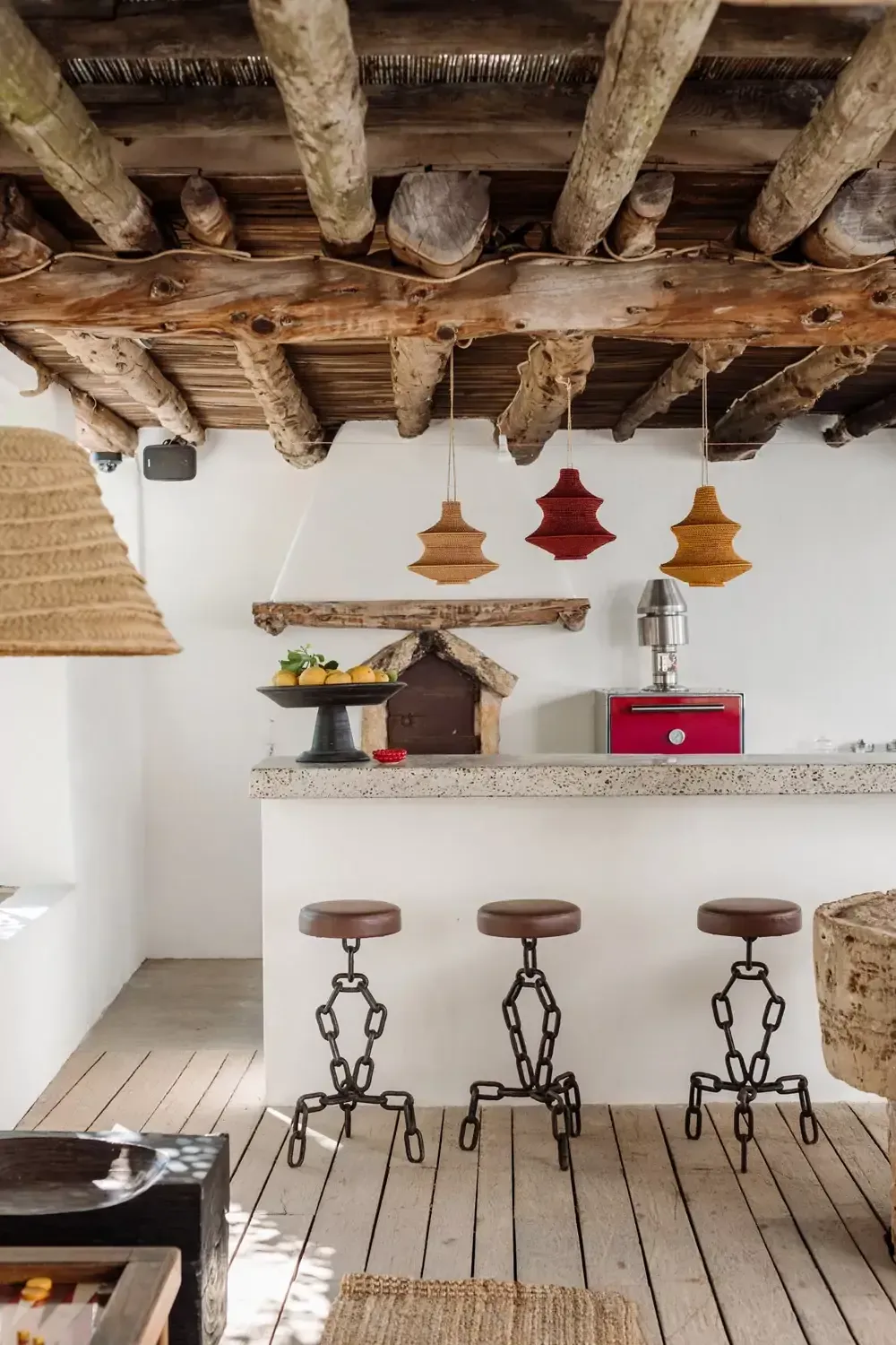 Finca La Inika, Balearic Islands, Spain — Rustic kitchen with exposed wooden beams, concrete countertop, woven pendant lights, and industrial bar stools.