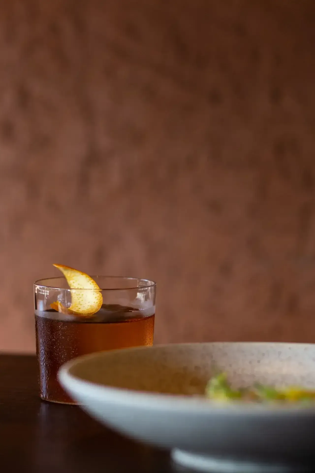 Further Hotel, Asia — Amber cocktail with pear garnish beside ceramic bowl on warm terracotta surface, soft natural light and minimalist plating.