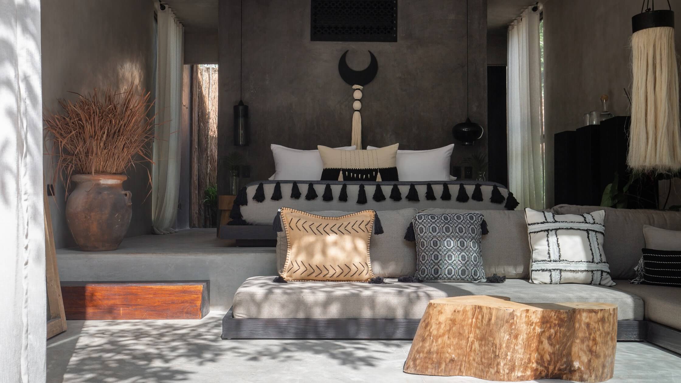 Bardo, Mexico — Concrete bedroom with woven textiles, carved wooden details, and sunlit minimalist furnishings in earth tones and charcoal.