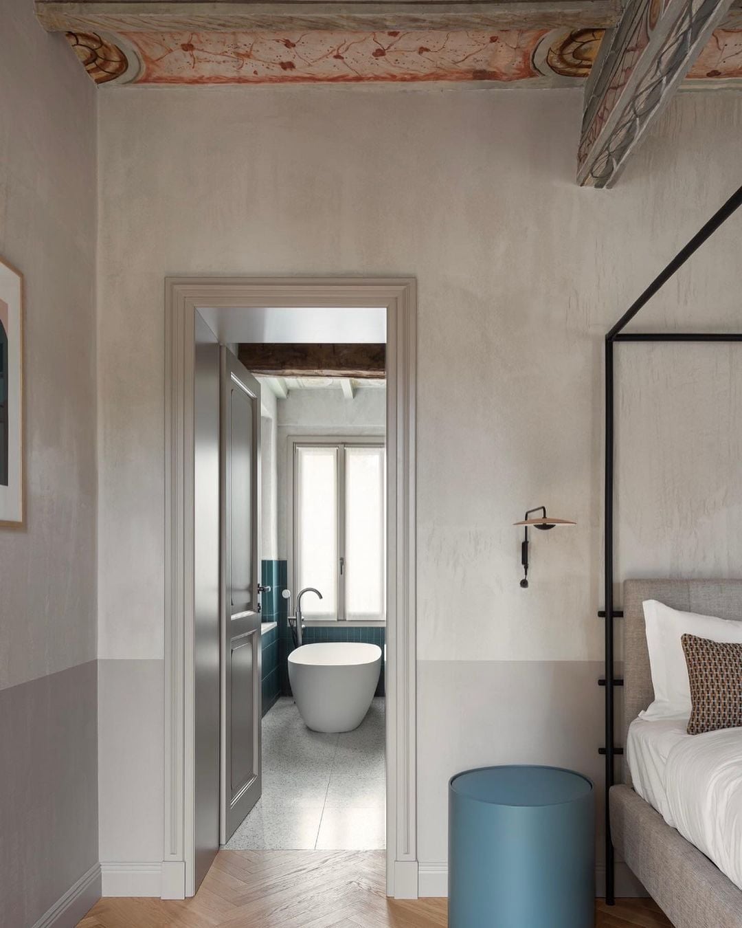 Roncolo 1888, Europe — Minimalist bedroom with ensuite bathroom, freestanding soaking tub, exposed timber ceiling beams, neutral palette with teal accents, natural light.