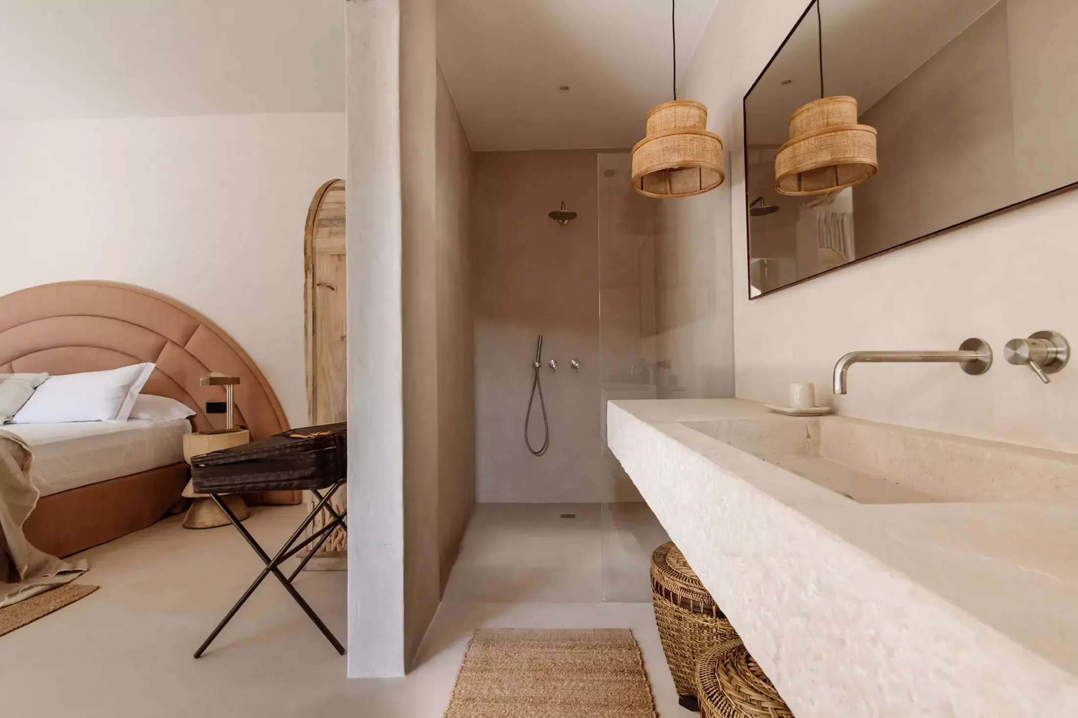 Finca La Inika, Balearic Islands — Ensuite bathroom with travertine sink, rattan pendants, walk-in shower, and adjoining bedroom with terracotta headboard.