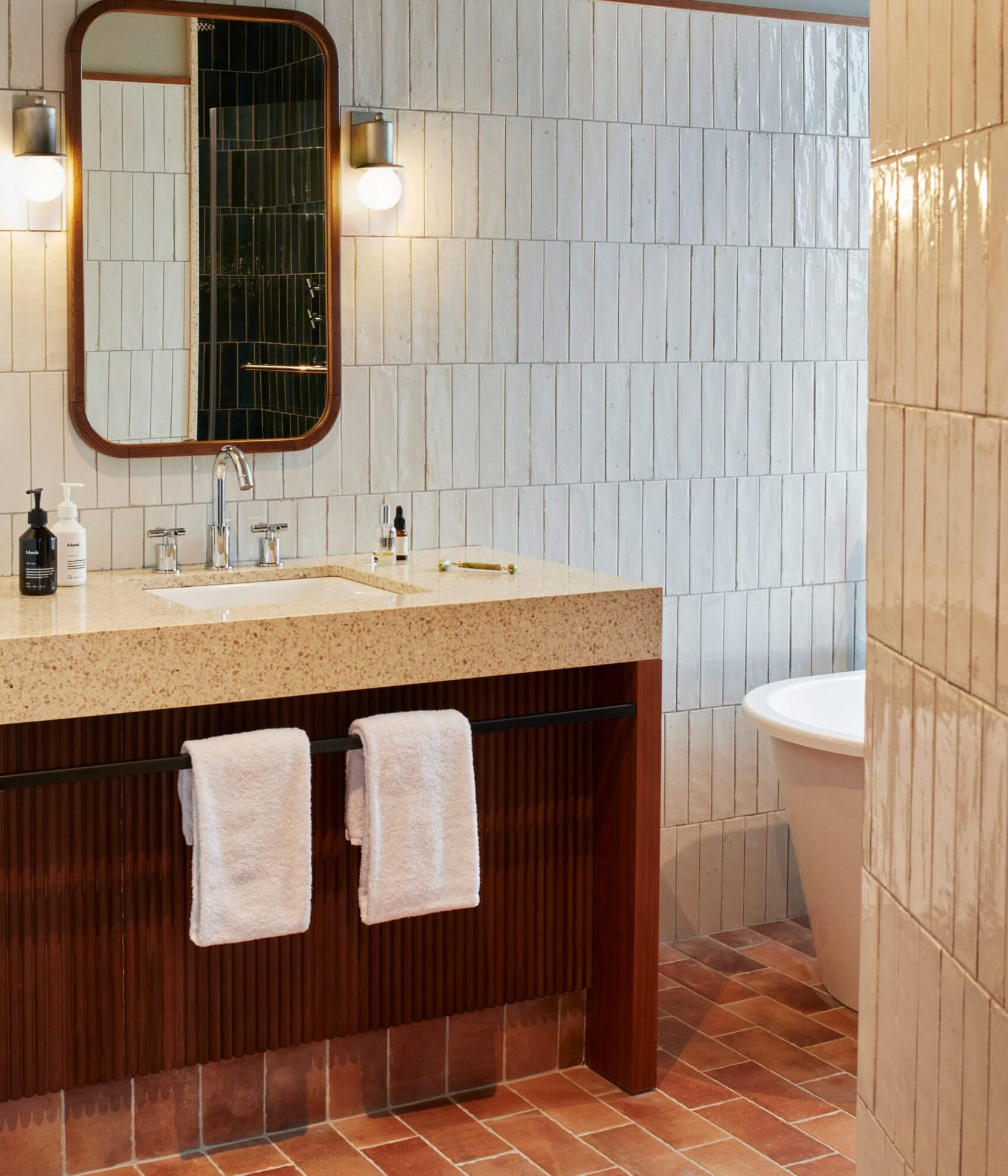 The Hoxton Poblenou, Barcelona, Spain — Bathroom with terrazzo countertop, dark wood vanity, vertical subway tile walls, brass-framed mirror, and terracotta floor.