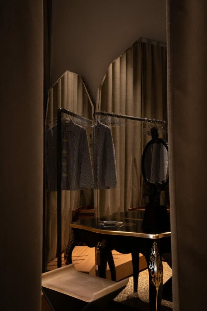 The Venice Venice Hotel, Europe — Luxury dressing room with mirrored closet, striped blazers on brass rail, warm ambient lighting, and marble-topped vanity with ornate black legs.
