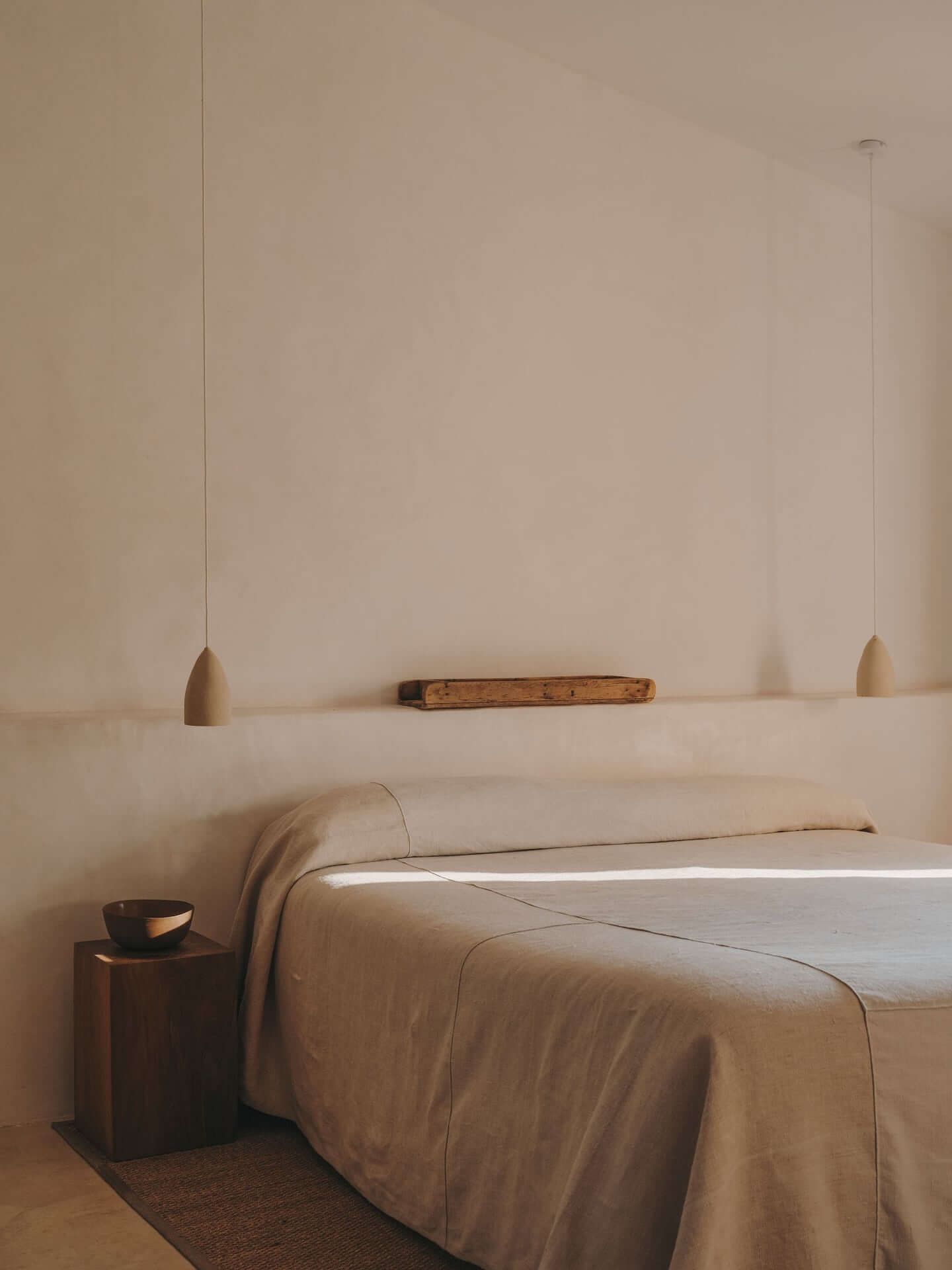 Can Lluïssó, Balearic Islands, Spain — minimalist bedroom with natural linen bed, wooden nightstand, pendant lights, and neutral plaster walls with warm Mediterranean light.