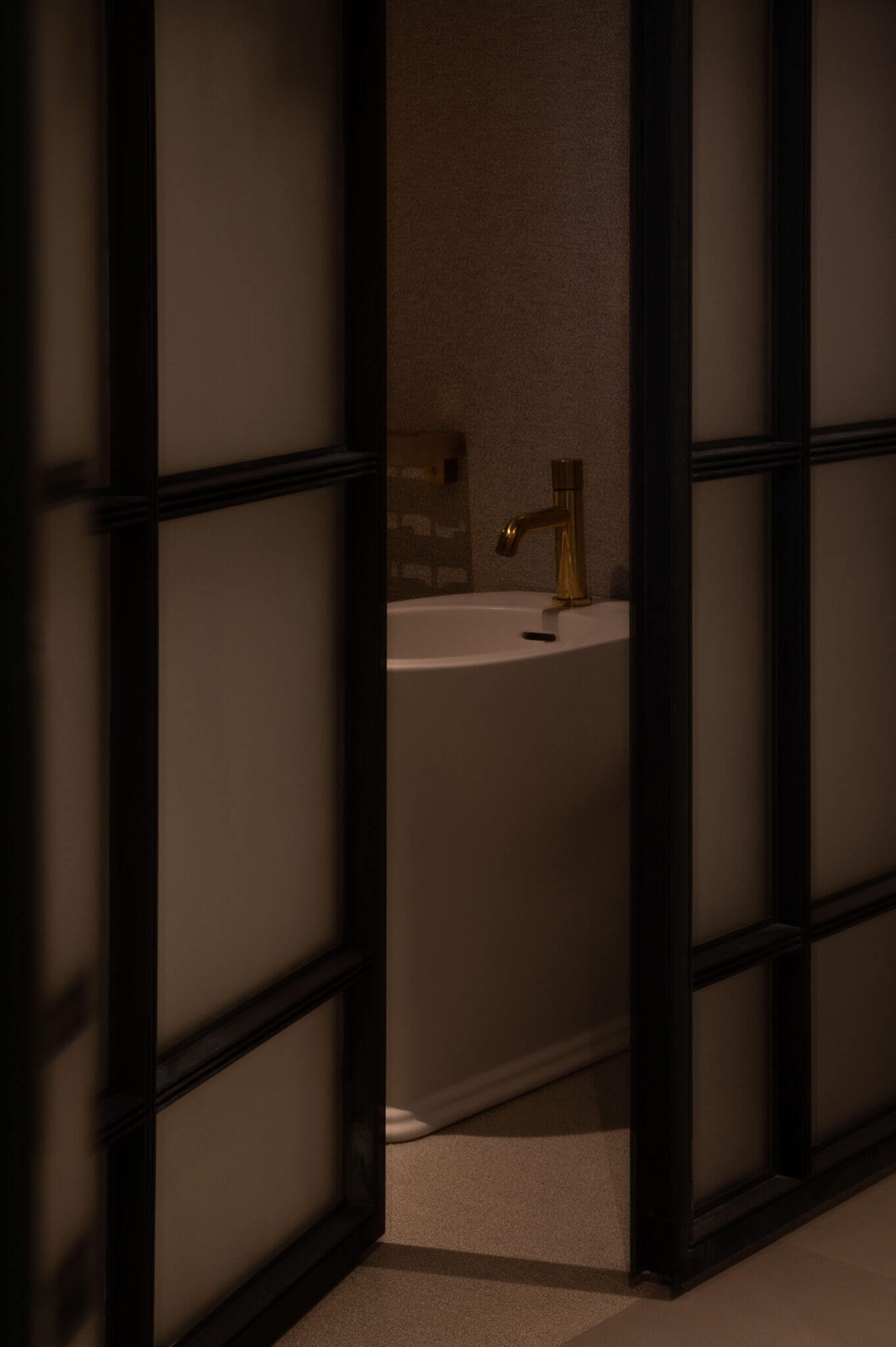 The Venice Venice Hotel, Europe — Modern bathroom with freestanding white bathtub, brass faucet, and frosted glass partition with black frame creating minimalist luxury spa aesthetic.