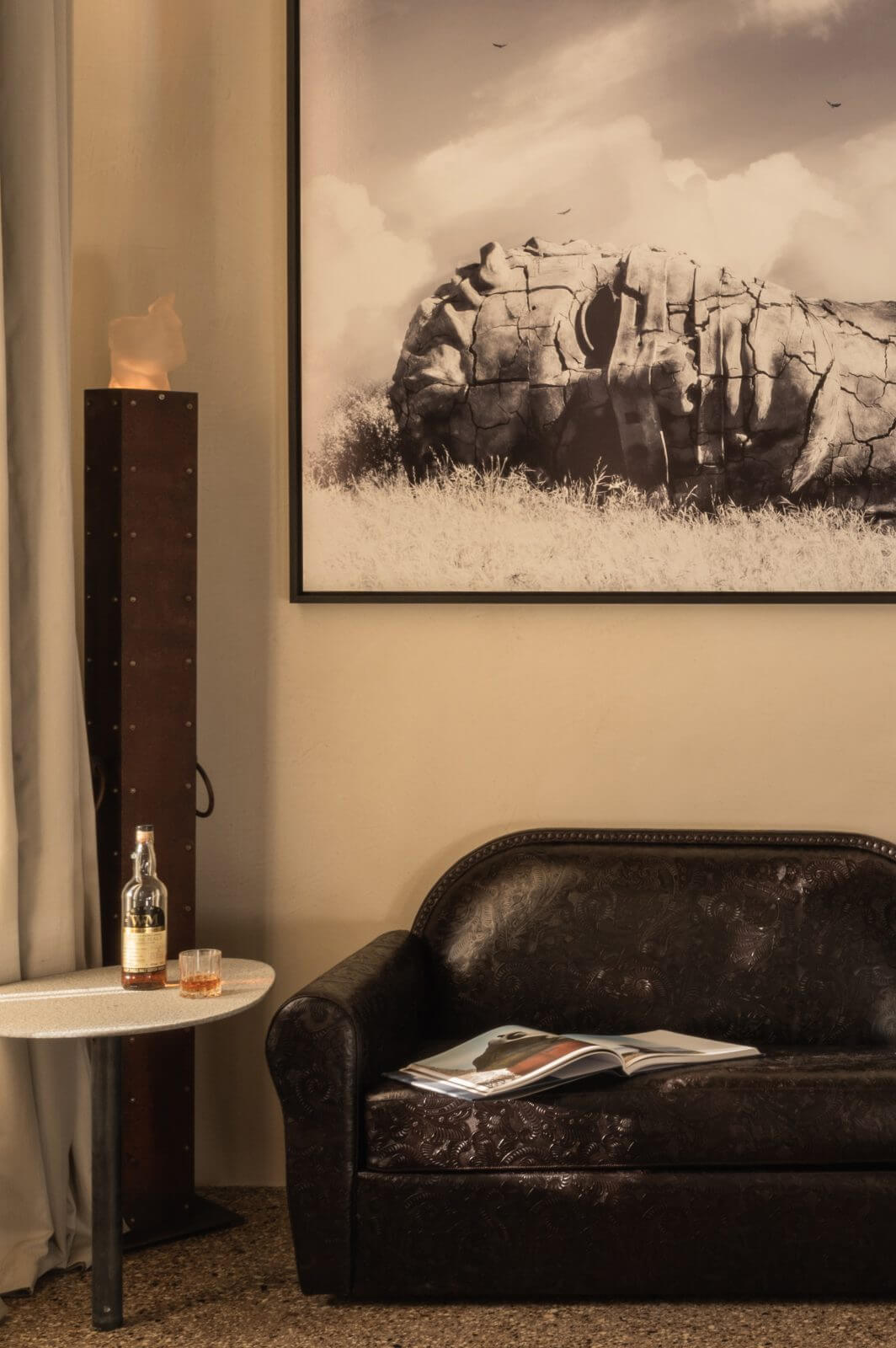 The Venice Venice Hotel, Europe — Black leather sofa with sepia-toned desert rock photograph, marble side table with whiskey bottle, minimalist luxury hospitality interior.