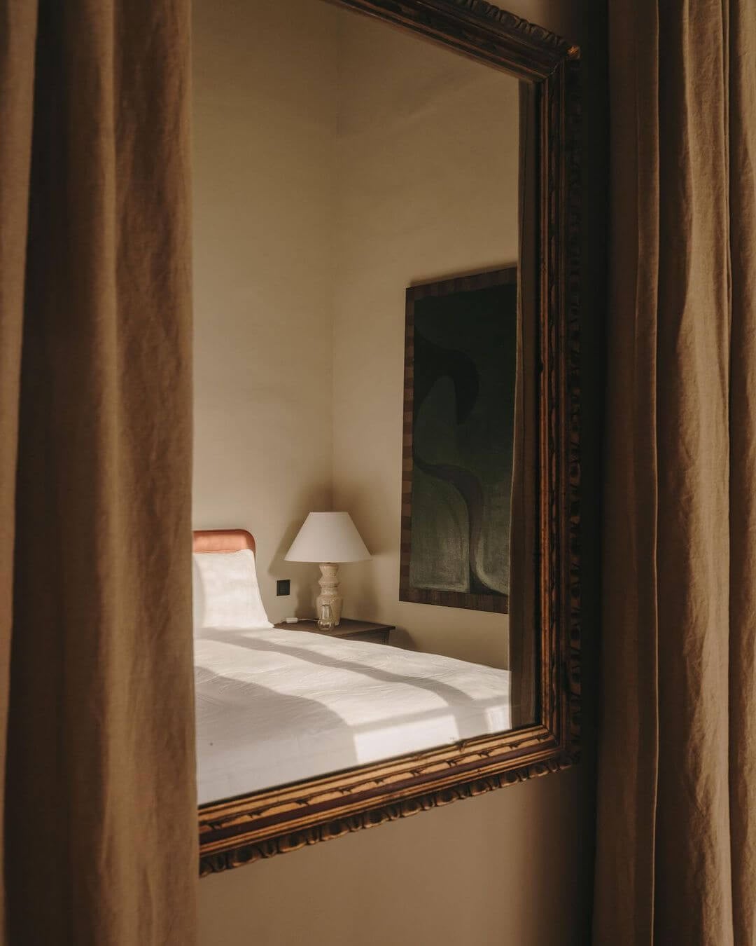 Santa Teresa 34, Balearic Islands — Ornate mirror reflects minimalist bedroom with natural light, neutral palette, and carved wooden frame detailing.