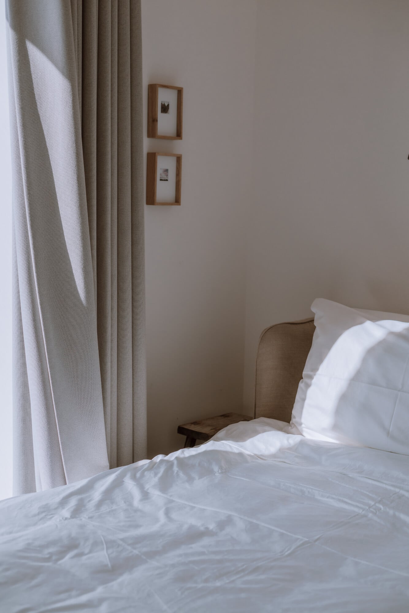 Villa Quercia, Italy — Minimalist bedroom with crisp white linens, taupe linen curtains, wooden-framed prints, and warm natural light from window.
