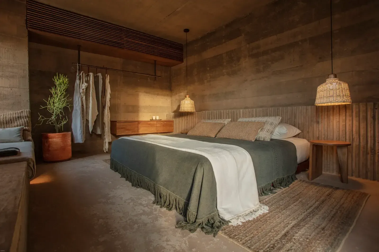 Paradero Todos Santos, Mexico — Minimalist bedroom with woven pendant lights, concrete walls, natural linen bedding, wooden furnishings, and warm earthy tones creating serene desert luxury aesthetic.