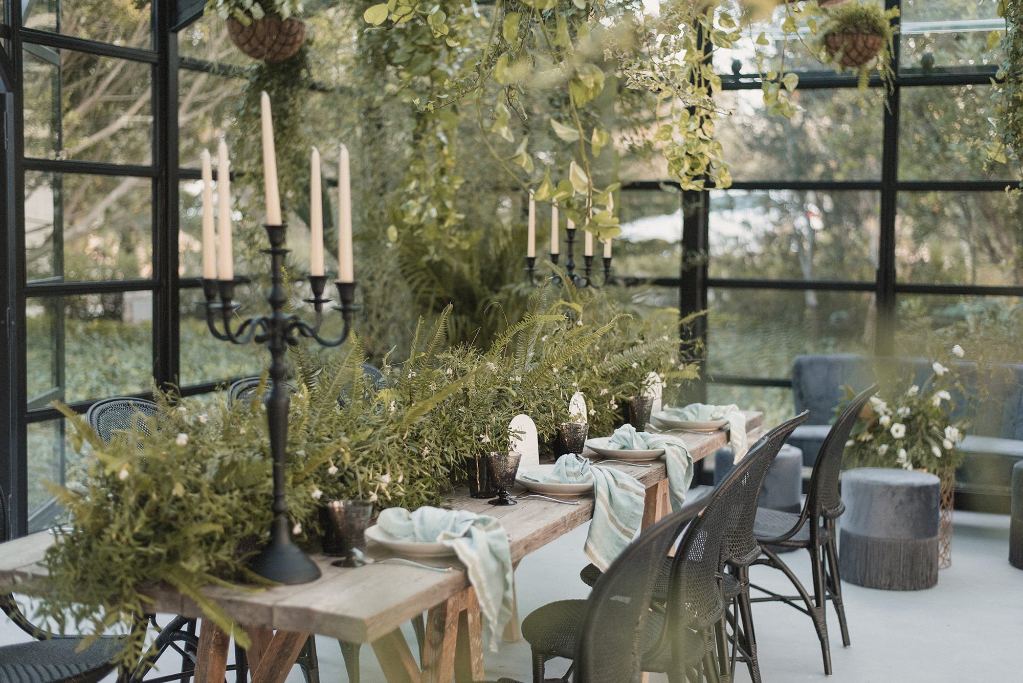 Finca Serena, Balearic Islands, Spain — Conservatory dining room with black-framed windows, botanical installations, candlelit candelabras, and garden views.