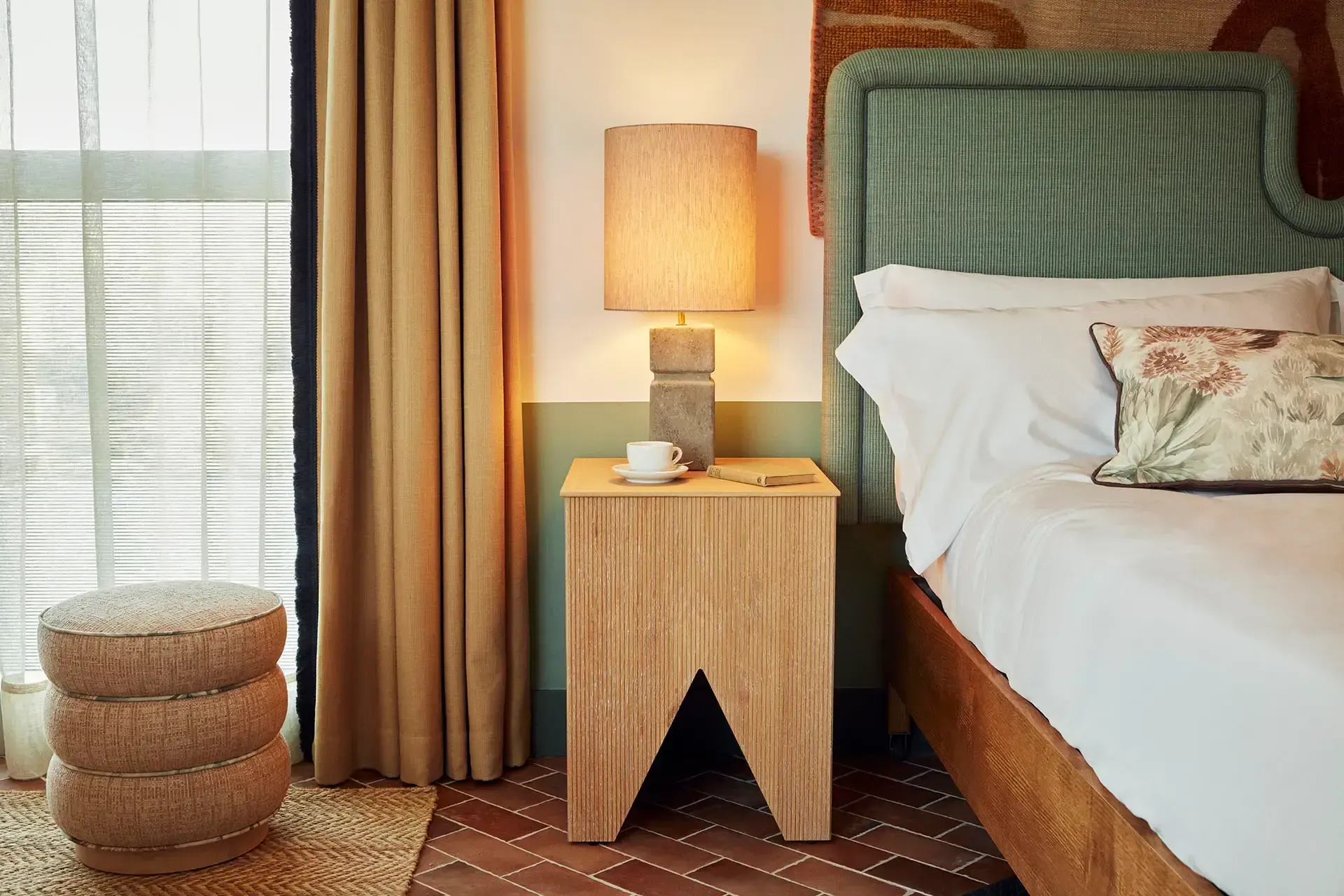 The Hoxton Poblenou, Barcelona, Spain — Bedroom with sage green upholstered headboard, wooden nightstand with lamp, terracotta floor tiles, and warm golden curtains.