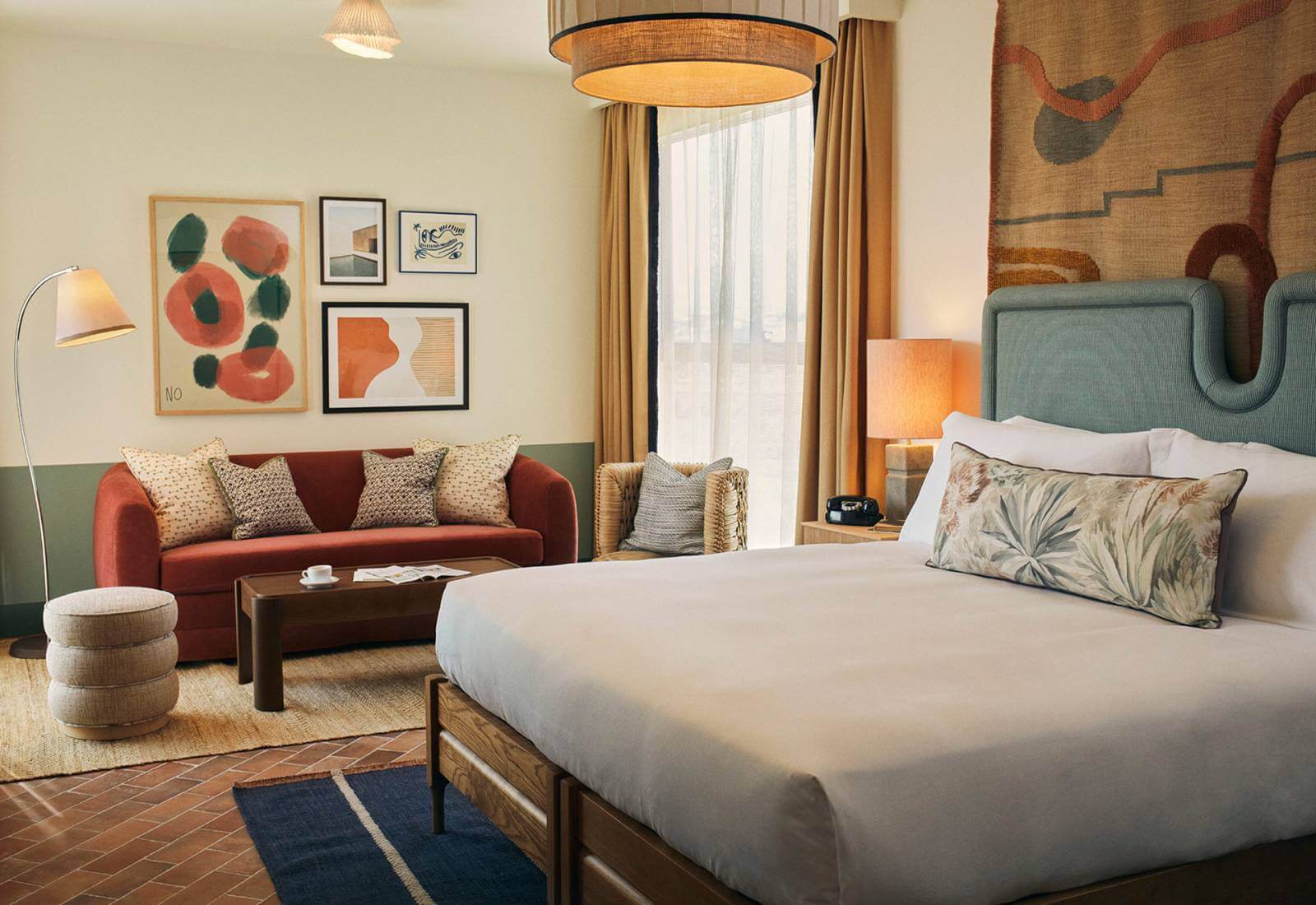 The Hoxton Poblenou, Barcelona, Spain — Modern hotel suite with sage green headboard, rust sofa, abstract artwork, warm lighting, and terracotta tile flooring.