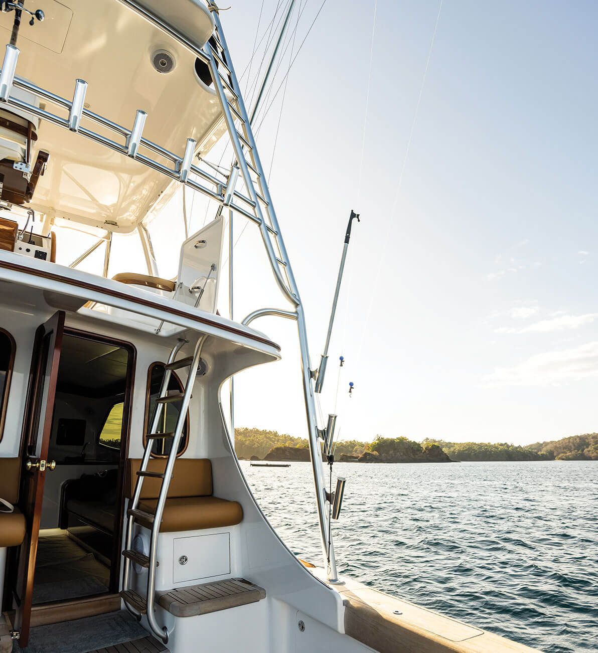 Boat Tour — Luxury sport fishing yacht with teak and chrome details anchored in calm coastal waters, tropical shoreline visible beyond.