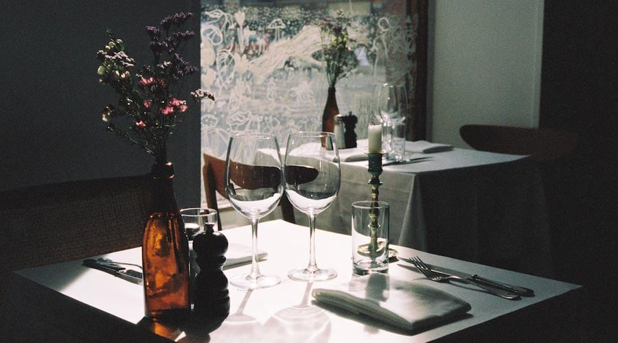 Svartengrens, Europe — Elegant fine dining table set with wine glasses, fresh flowers, candlelight, and soft natural window light creating intimate upscale restaurant atmosphere.