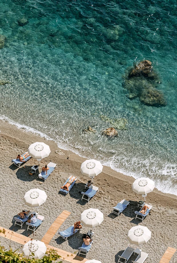 Borgo Santandrea, Europe — Aerial view of pristine sandy beach with striped loungers, white umbrellas, and turquoise Mediterranean waters with rocky outcrops.