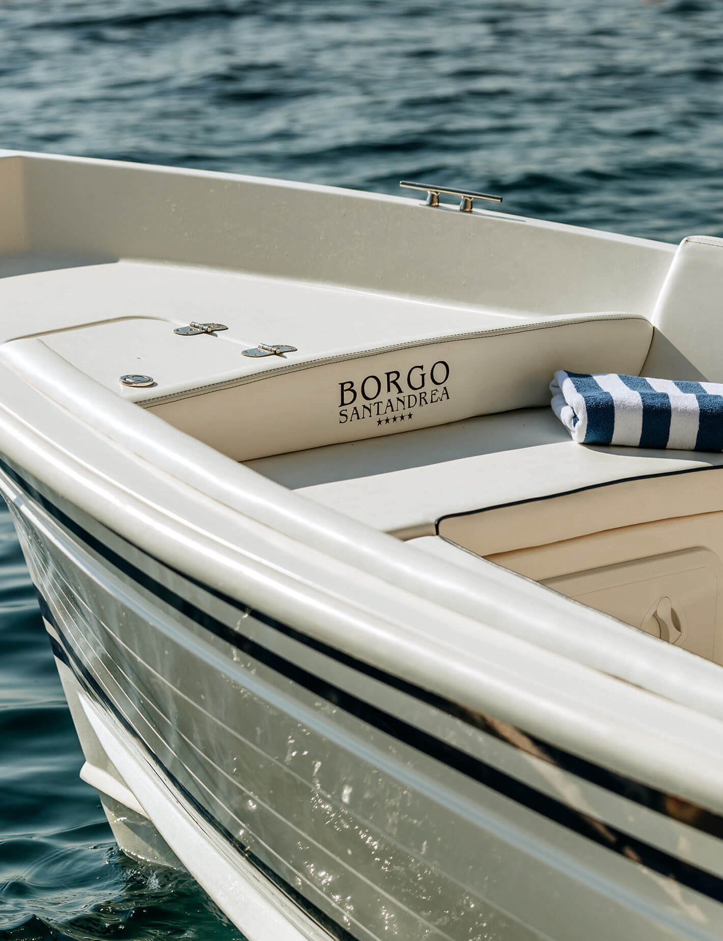Borgo Santandrea, Europe — Luxury white motorboat with striped towel and branded cushion on calm Mediterranean waters, showcasing coastal leisure and refined nautical design.