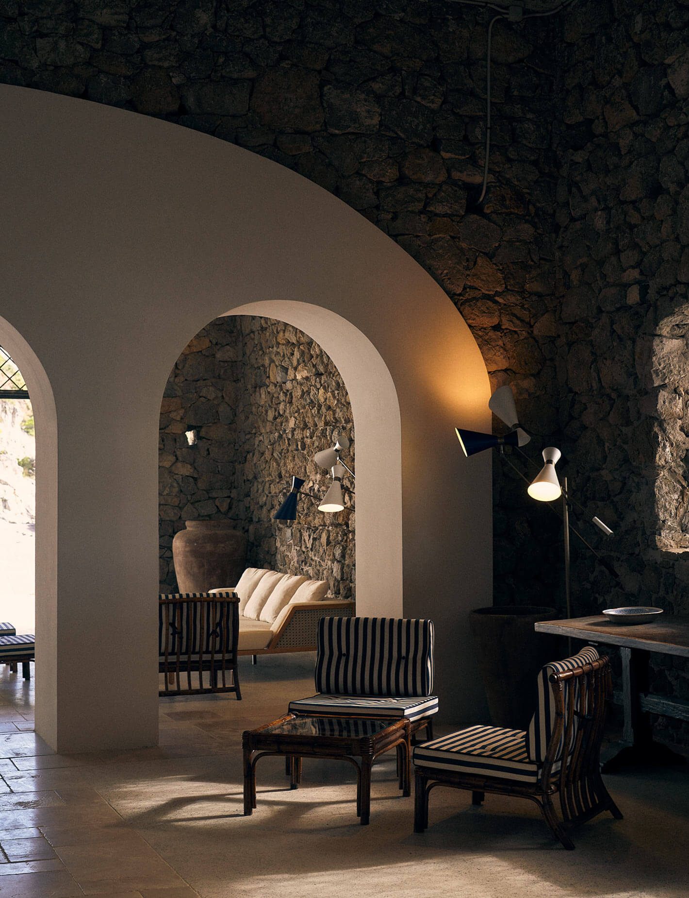 Borgo Santandrea, Europe — Stone archway framing striped chairs and sofa in modernist interior with barrel vault ceiling and warm ambient lighting.