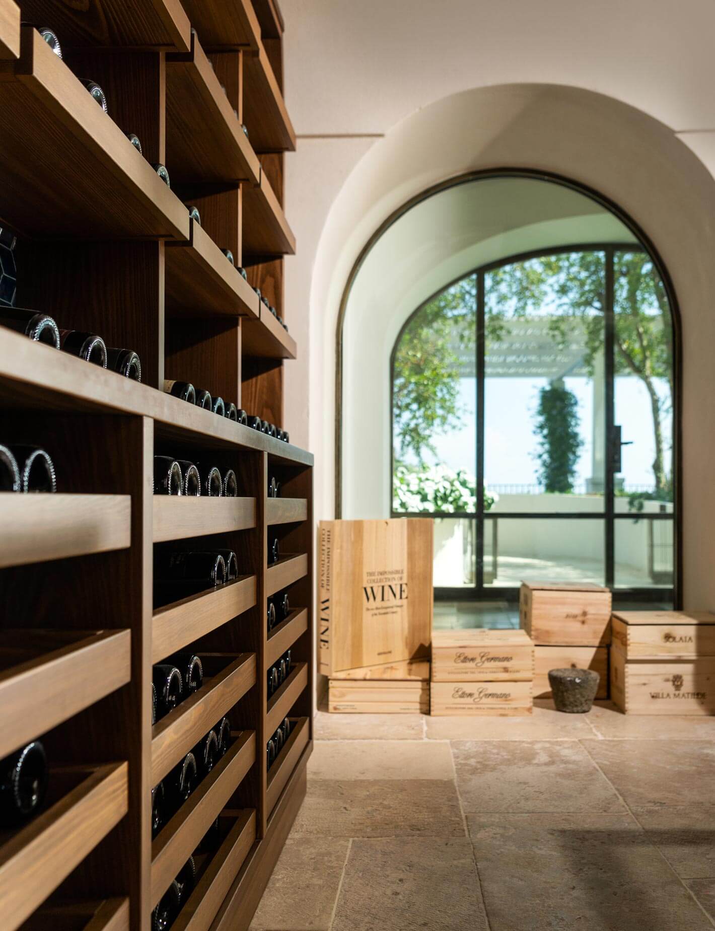 Wine Cellar, Europe — Arched cream doorway frames lakeside view beside wooden wine storage shelves with black labels and stacked vineyard crates on stone floor.