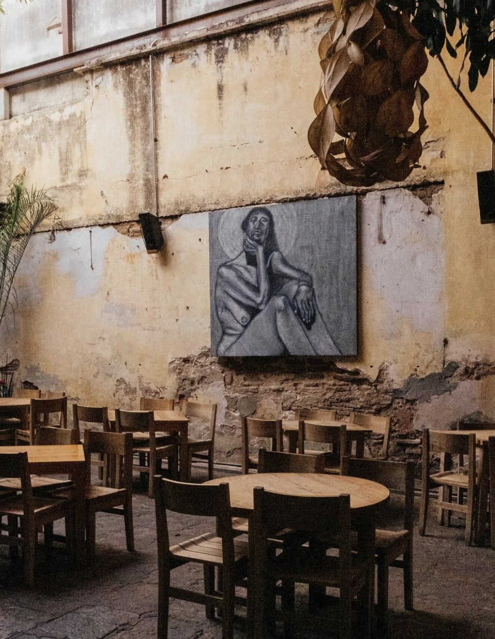 Boulenc, Mexico — Weathered courtyard with wooden tables, charcoal portrait sketch on aged wall, climbing vines, natural light, rustic hospitality aesthetic.