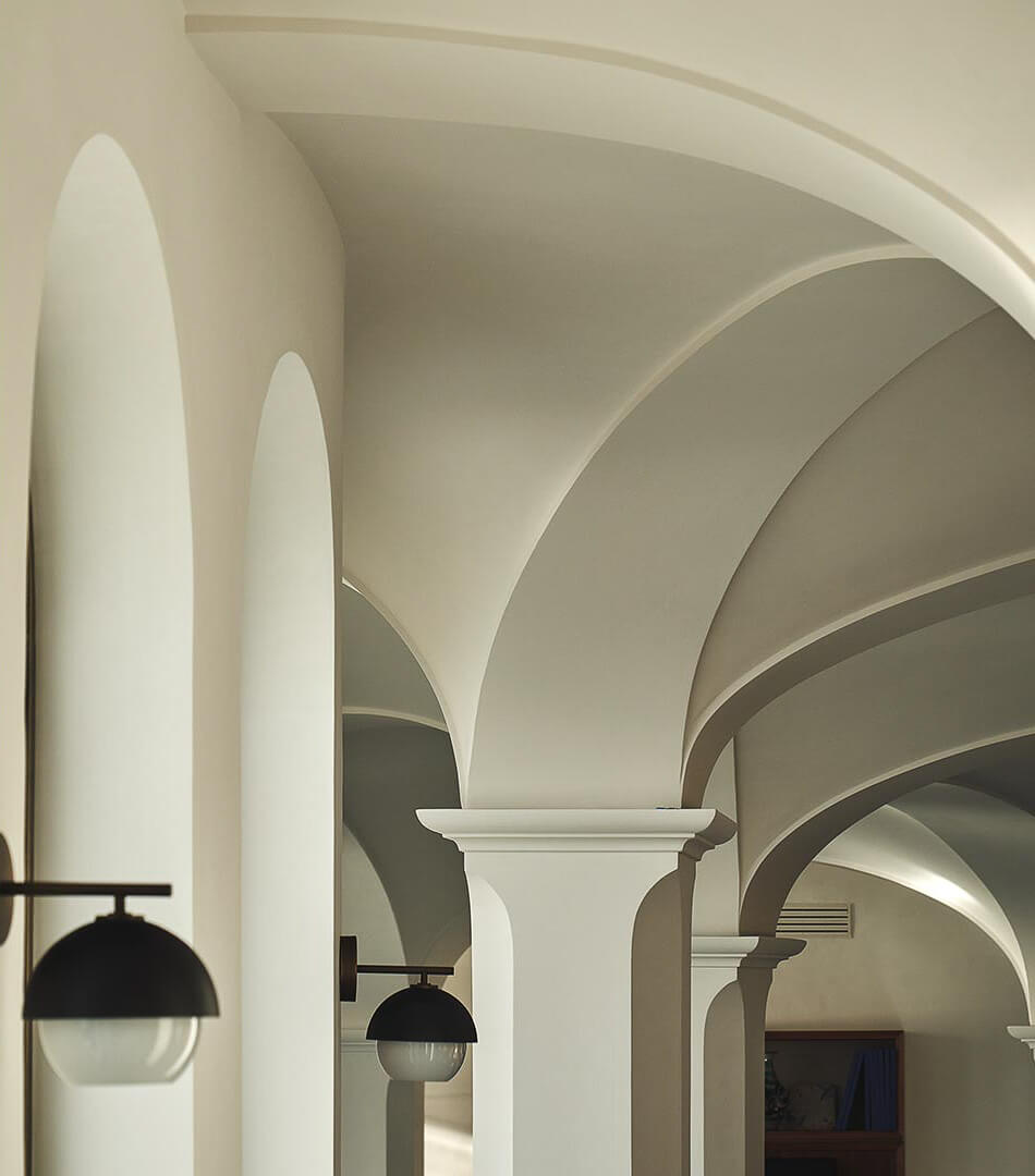 Borgo Santandrea, Europe — Arched corridors with cream plaster vaults, cylindrical columns, and suspended black pendant lighting creating Mediterranean neoclassical architecture.
