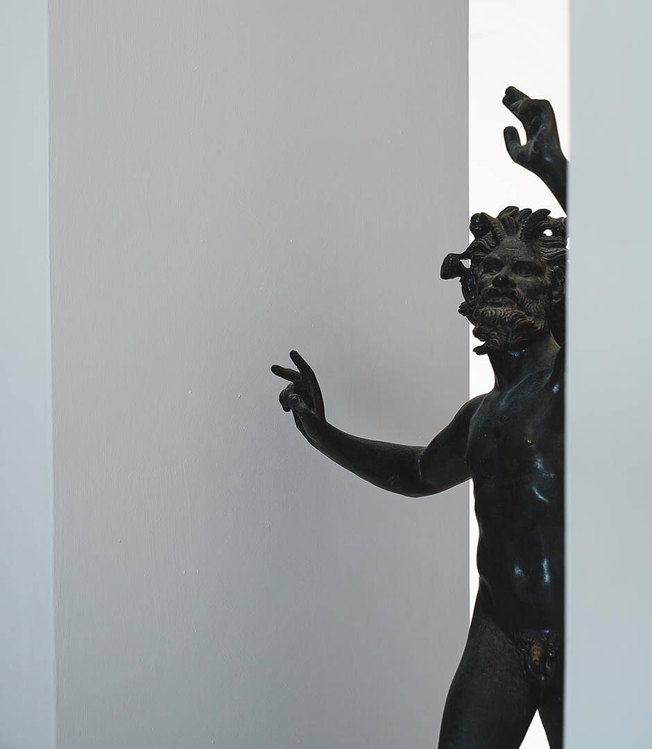 Borgo Santandrea, Europe — Black bronze sculptural figure with expressive gesture emerging from white architectural niche, classical art detail.