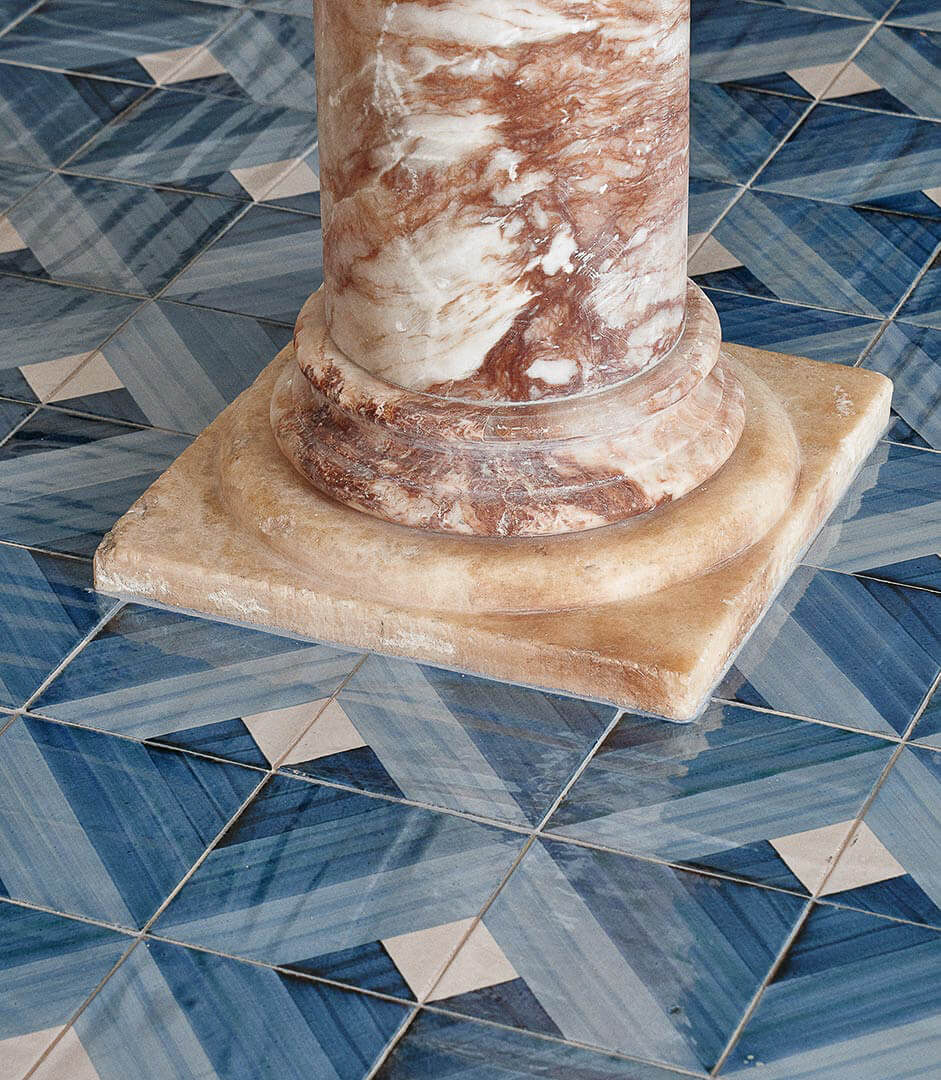 Borgo Santandrea, Europe — Travertine column base on geometric blue and cream tile flooring, architectural detail in luxury hospitality setting.