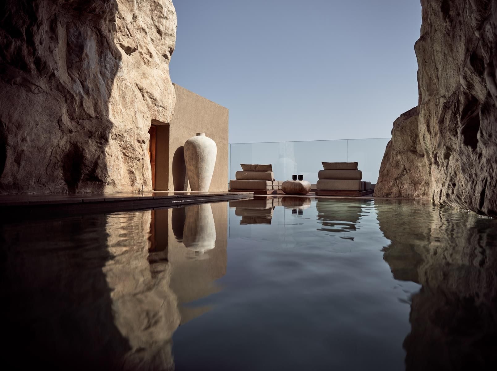 ACRO Suites, Europe — Minimalist poolside pavilion nestled between limestone cliffs, featuring cream vessel sculpture, stacked linens, and still water reflection under clear sky.