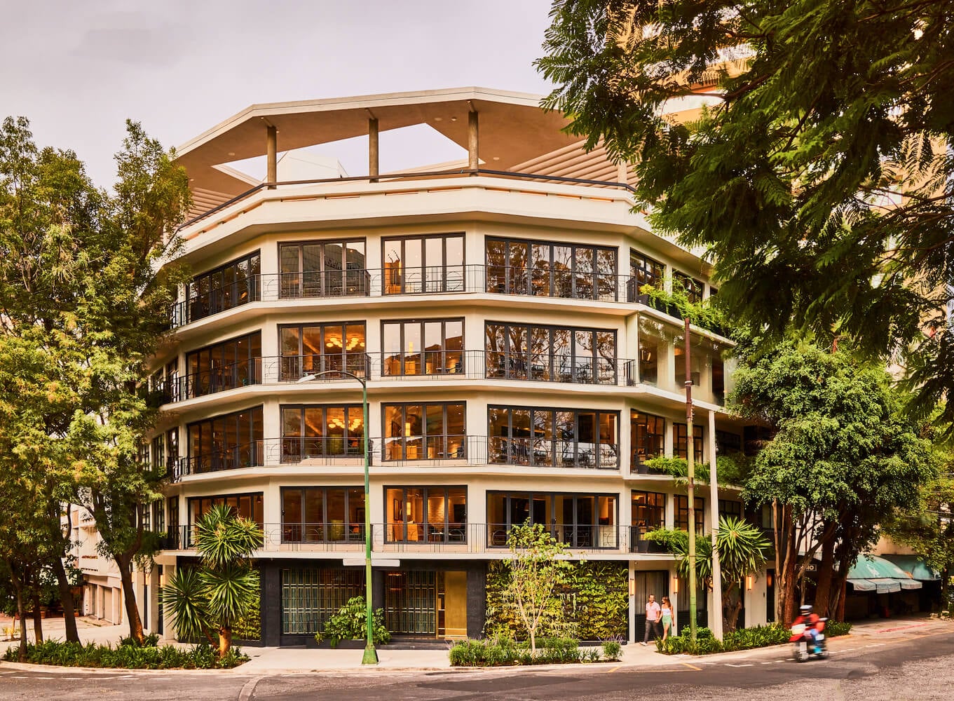 Campos Polanco, Mexico — Curved modernist residential tower with stacked balconies, warm wood interiors, and lush street-level landscaping in afternoon light.