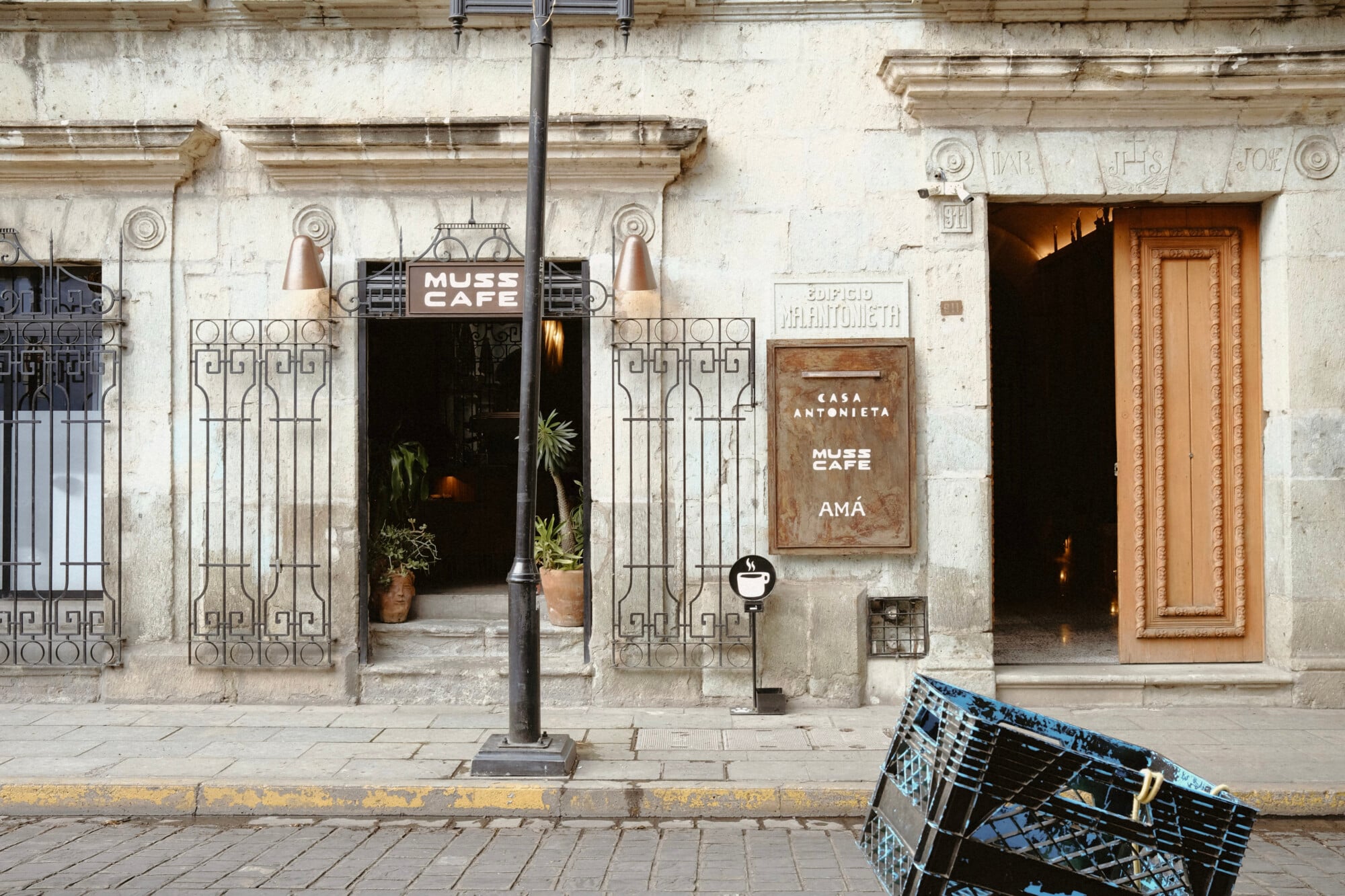 Casa Antonieta, Mexico City, Mexico — Neoclassical facade with ornamental ironwork, cream stone exterior, brass sconces, potted palms, and street-level cafe entrance.