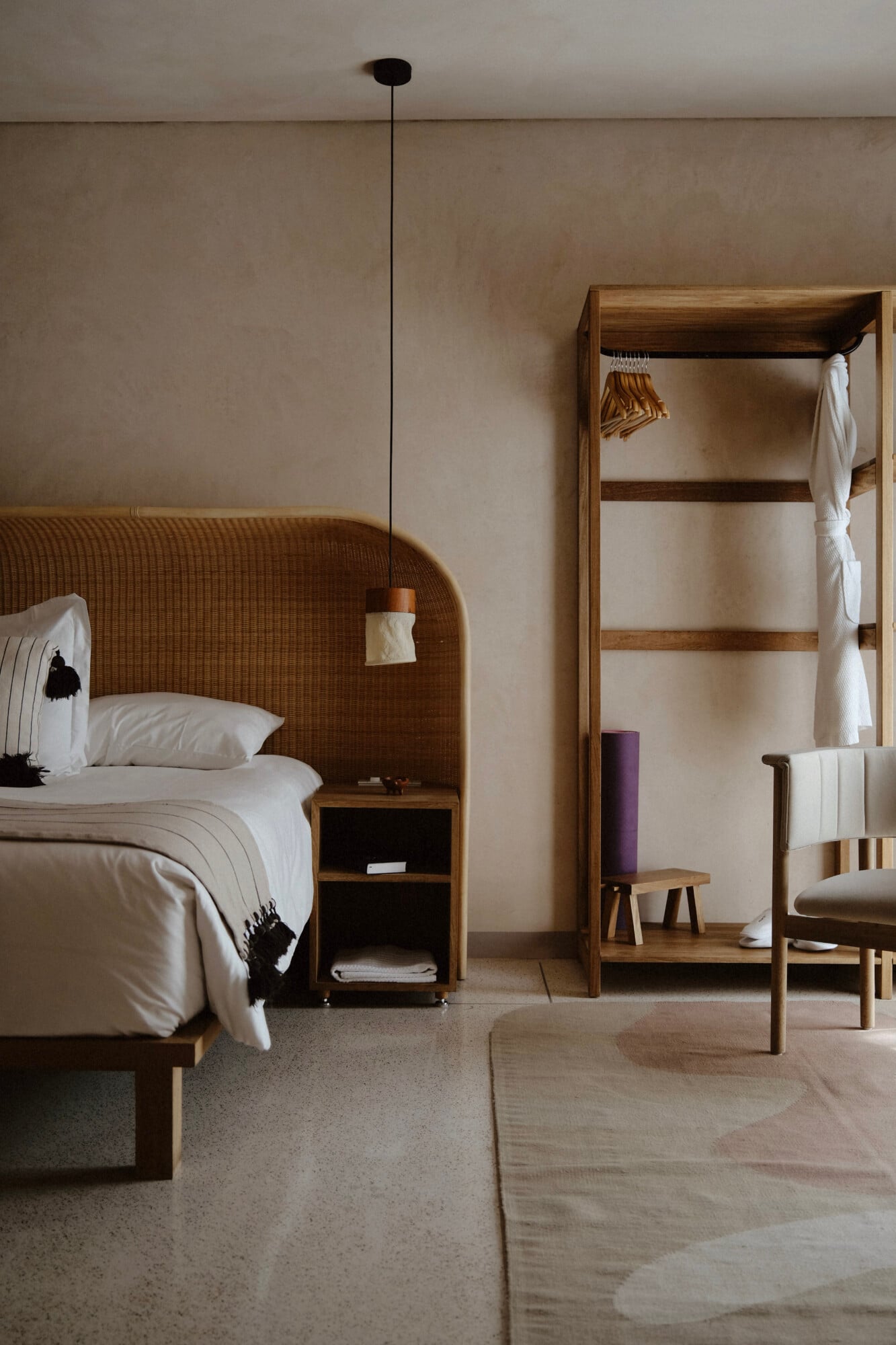 Casa Antonieta, Mexico — Minimalist hotel bedroom with woven rattan headboard, wooden wardrobe, pendant light, and neutral palette of white linens and natural wood furniture.