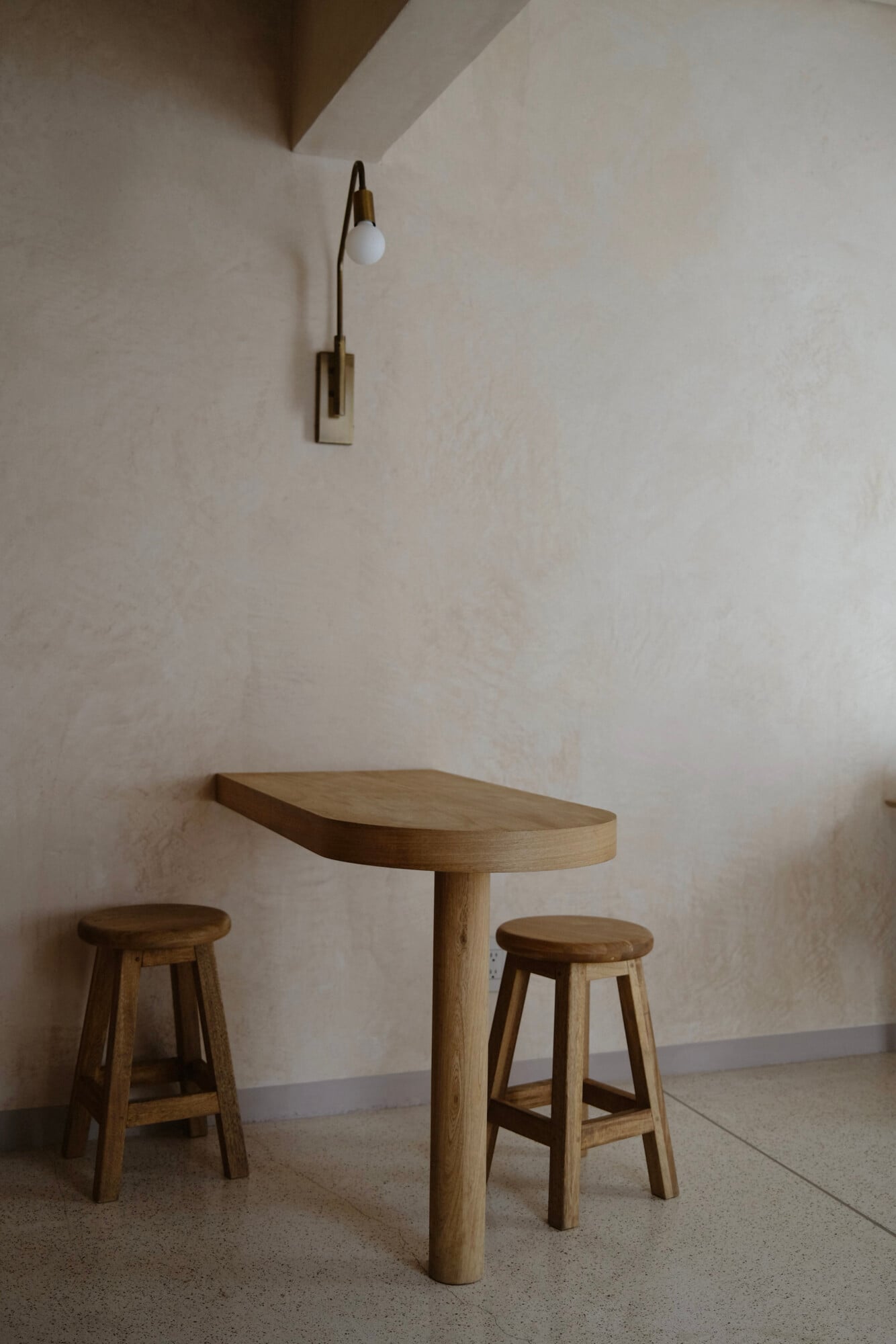 Casa Antonieta, Mexico — Minimalist wooden bar table with curved top and two stools beneath brass arc wall lamp in whitewashed room.