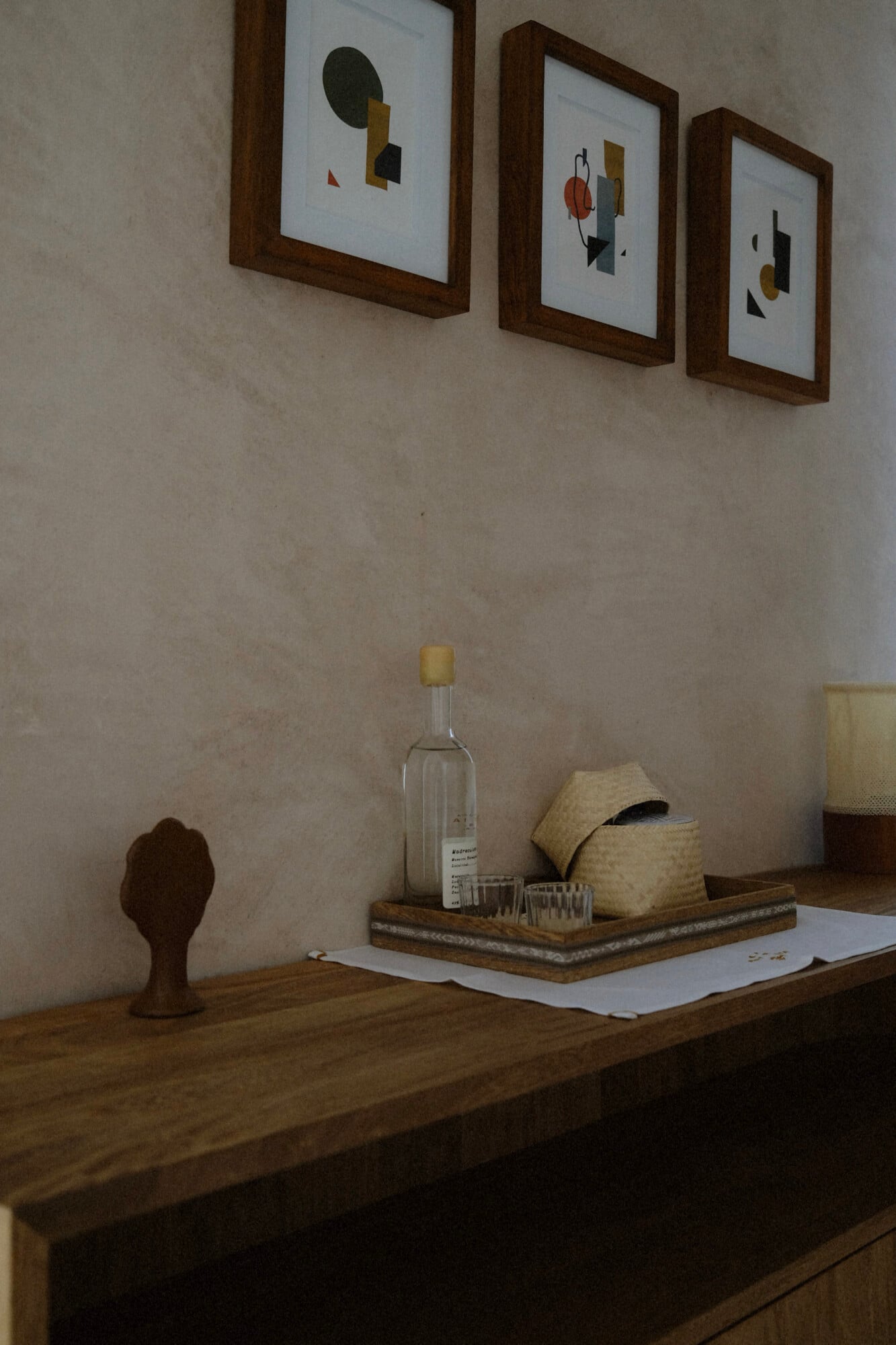 Casa Antonieta, Mexico — Minimalist wooden desk with glass bottle, woven basket, and small sculpture beneath three framed abstract artworks in natural light.