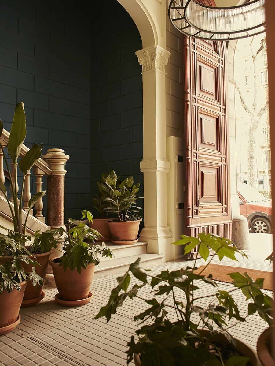 Casa Bonay, Europe — Sunlit courtyard with terracotta planters, classical columns, arched doorway, and warm stone architecture casting dramatic shadows.