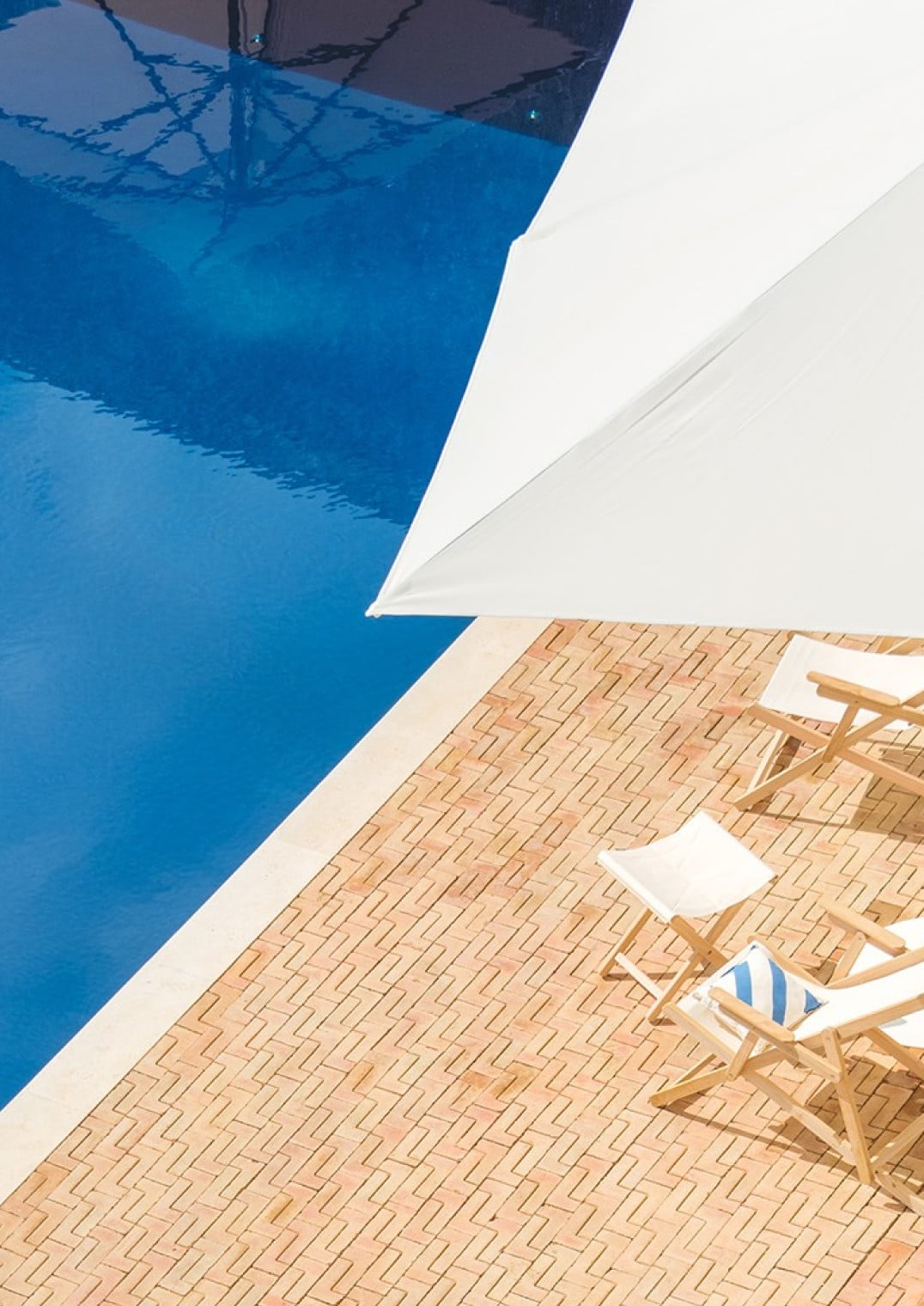Casa Mãe, Europe — Poolside terrace with wooden deck chairs, white sail shade, and azure water reflecting clear sky.