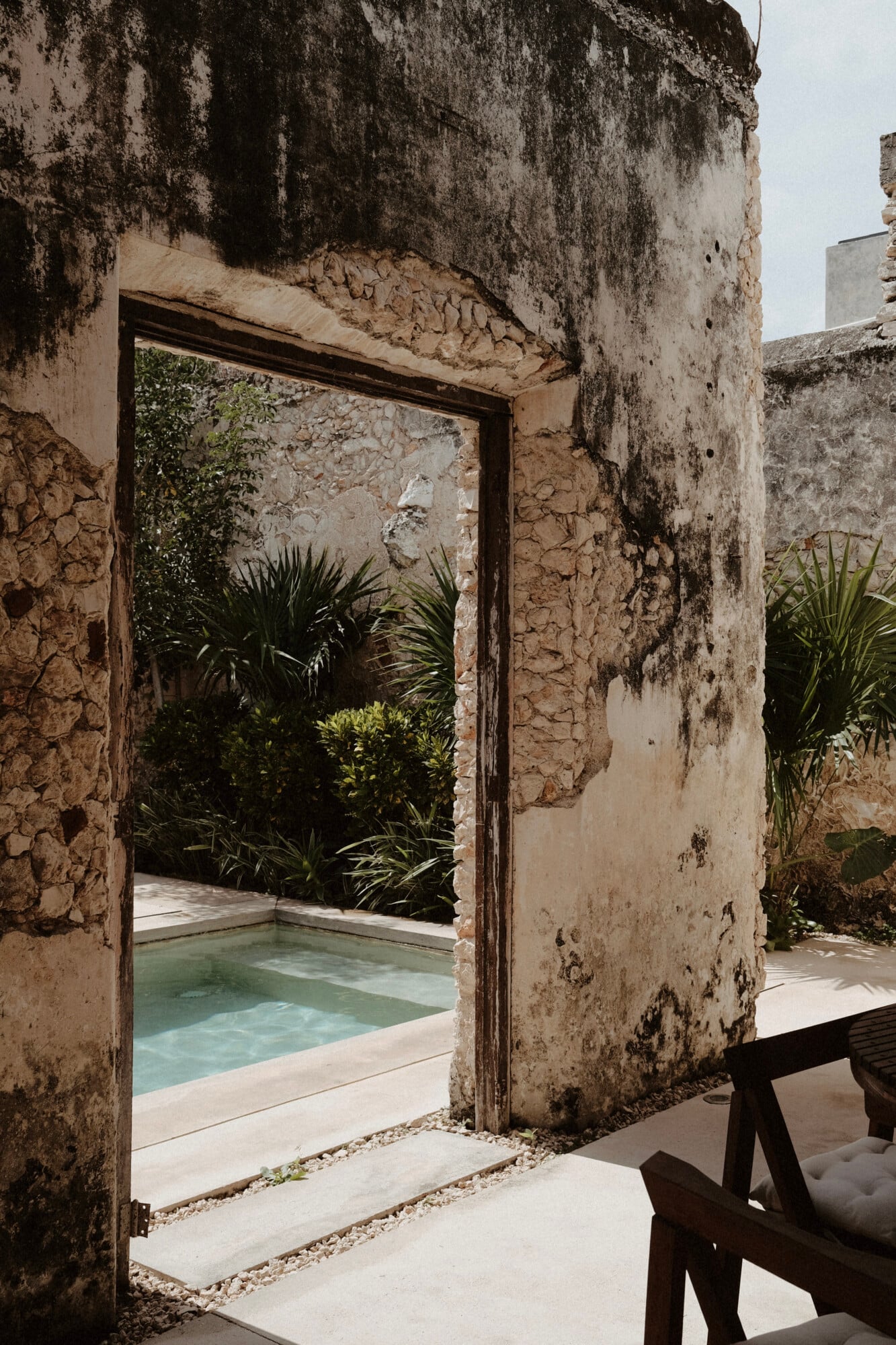 Casa Lohr, Mexico — Weathered stone archway framing turquoise pool and tropical plants, minimalist courtyard with modern design aesthetic.
