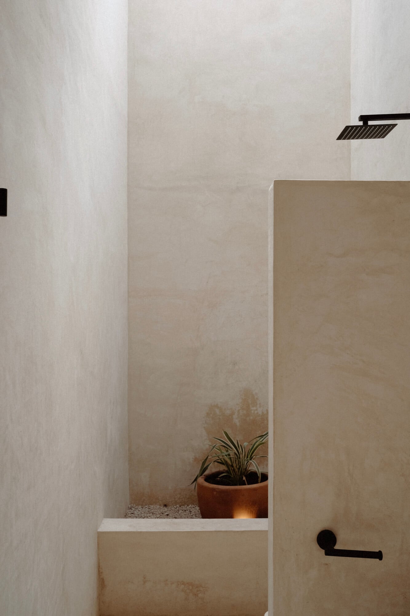 Casa Lohr, Mexico — Minimalist shower niche with terracotta plant pot, white plaster walls, black fixtures, and skylight in luxury villa bathroom.