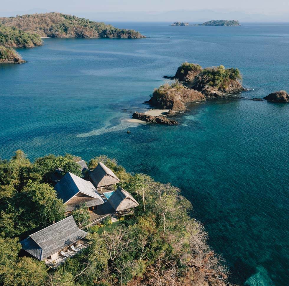 Islas Secas, Panama — Thatched-roof oceanfront pavilions nestled in tropical forest overlooking turquoise waters and forested islands under clear sky.