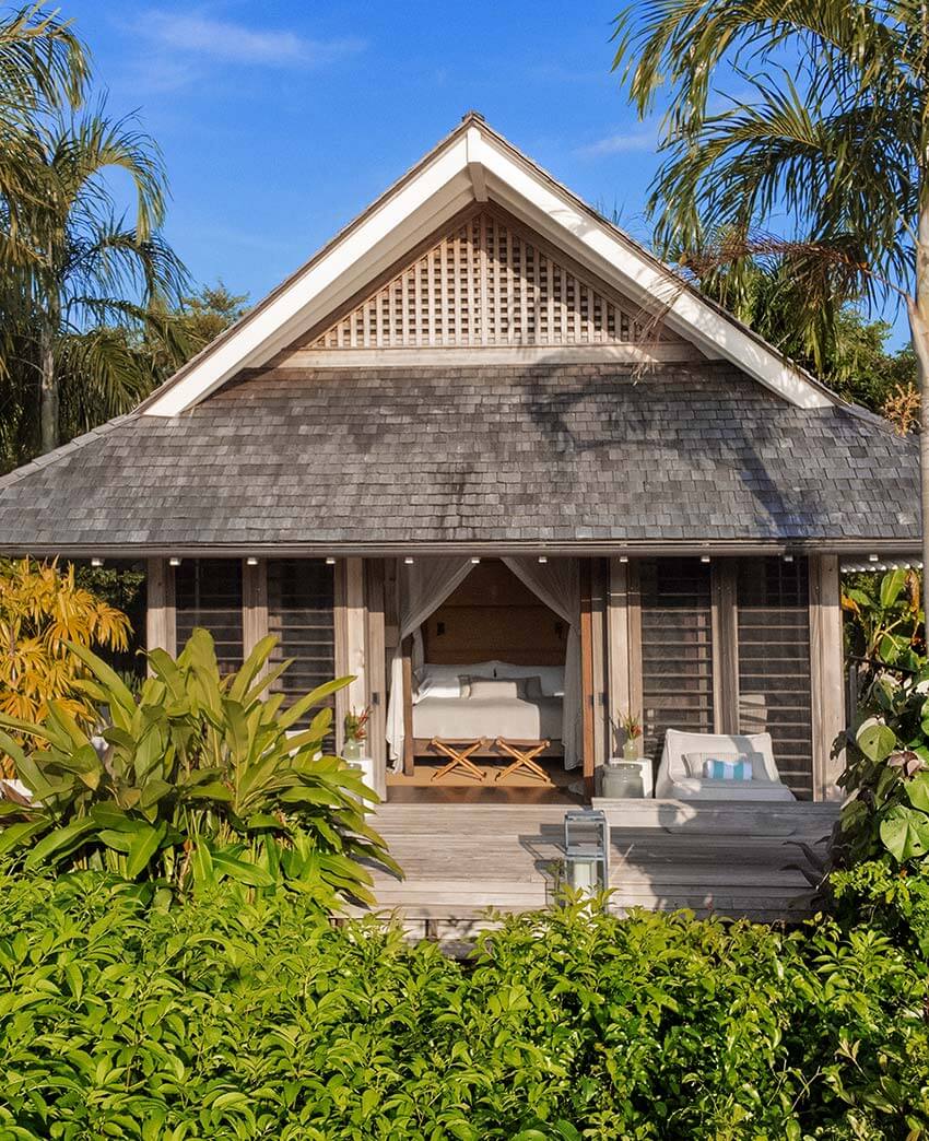 Islas Secas, Panama — Thatched-roof villa with dark shingle siding, latticed gable detail, and open-air bedroom pavilion surrounded by tropical palms and lush vegetation.