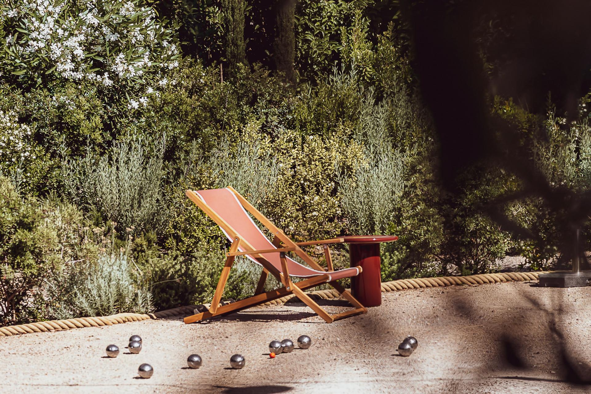 Hôtel Lou Pinet, Europe — Coral deck chair and bocce balls on sandy terrace surrounded by olive trees and rope railings.