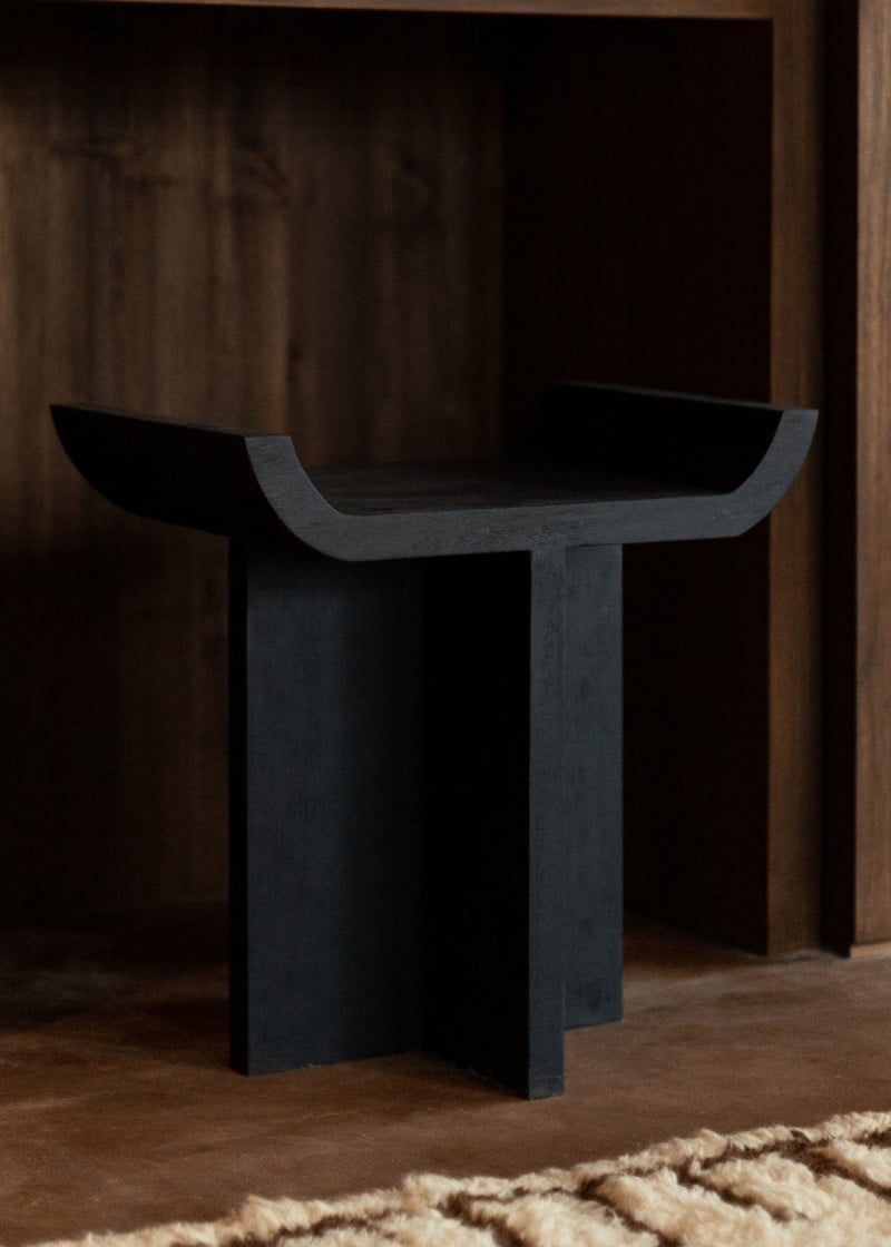 Further Hotel, Asia — Dark sculptural pedestal table with curved top and geometric base in minimalist interior with warm wood paneling and neutral textile.